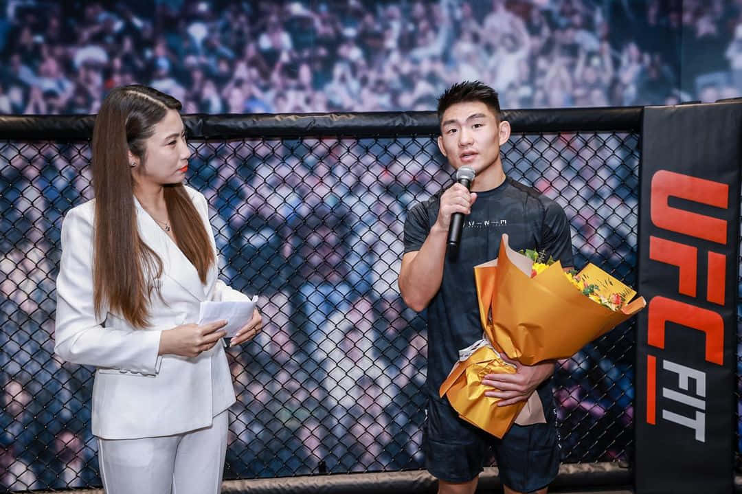 Athlete 桌布 壁紙 — 一名UFC拳手手持鮮花，在八角籠內與女記者交談，背景有觀眾。