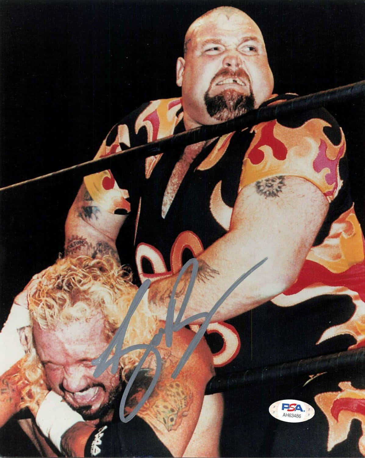 WWE 桌布 壁紙 — 一名光頭、留山羊鬍、穿火焰圖案襯衫的摔角手，在殘酷比賽中於擂台上抓住另一名摔角手。