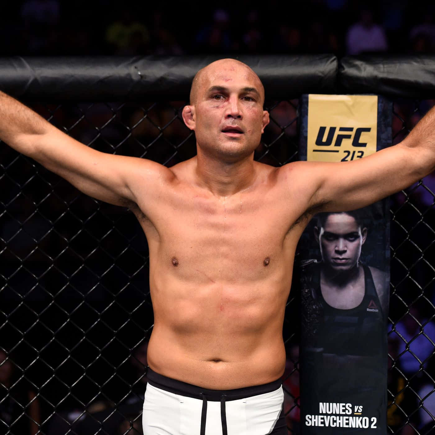 UFC 桌布 壁紙 — 一名光頭UFC拳手在八角籠中高舉雙臂，經過一場艱苦比賽後勝利地站立。
