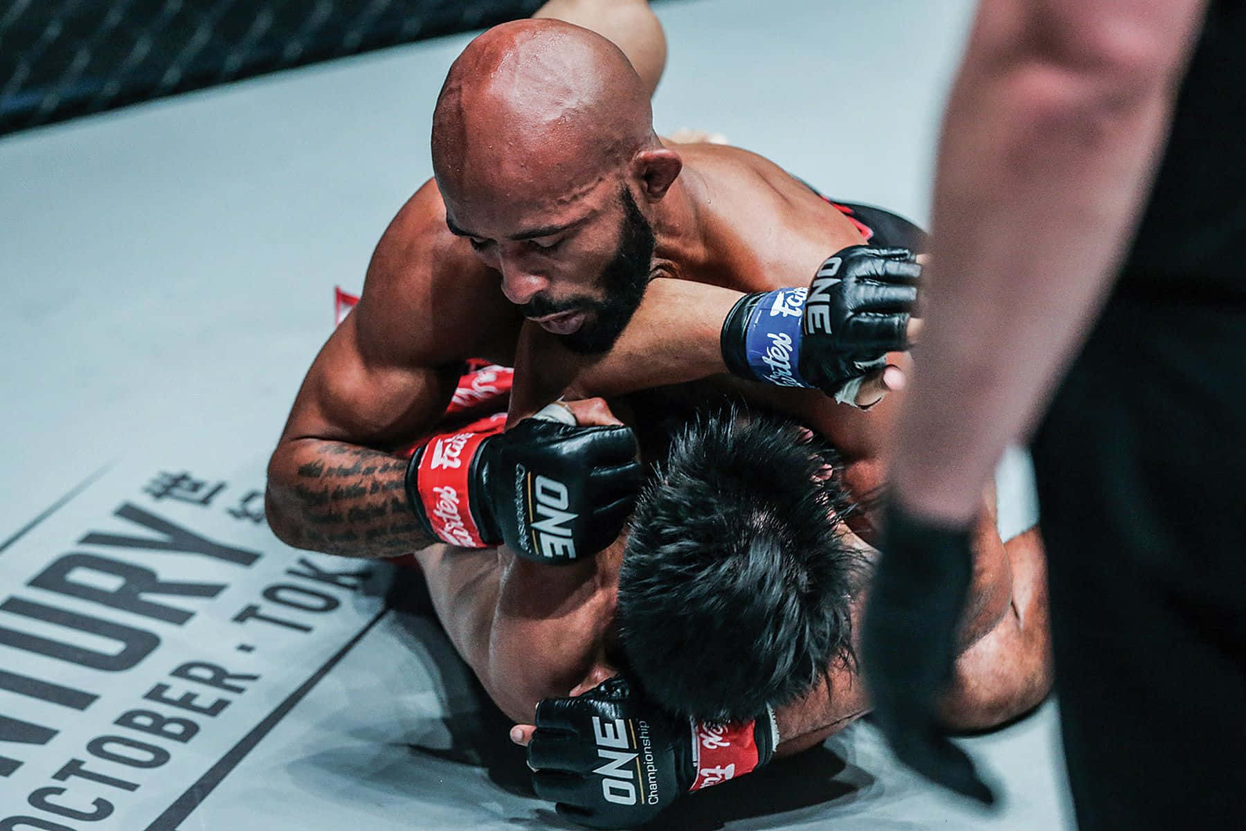 Champion 桌布 壁紙 — 一名光頭拳手戴著紅色手套，在ONE Championship擂台上於一場激烈的MMA寢技交鋒中壓制對手。