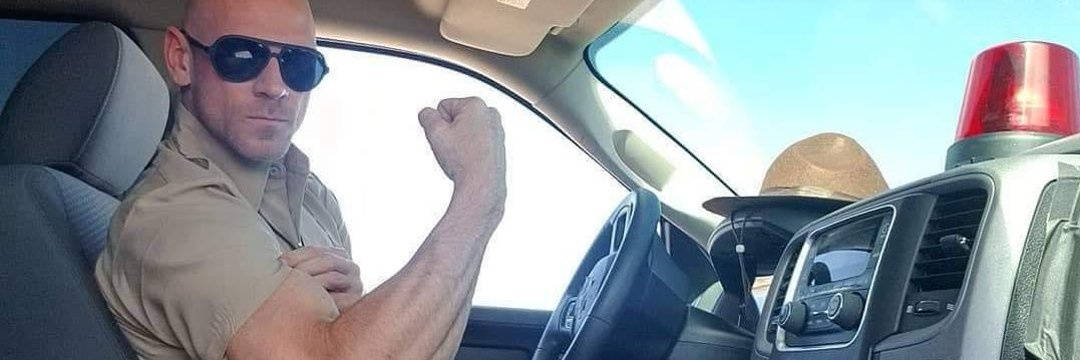 meme 桌布 壁紙 — 一名光頭男子戴著太陽眼鏡，在車頂有紅燈的警車內彎曲二頭肌。