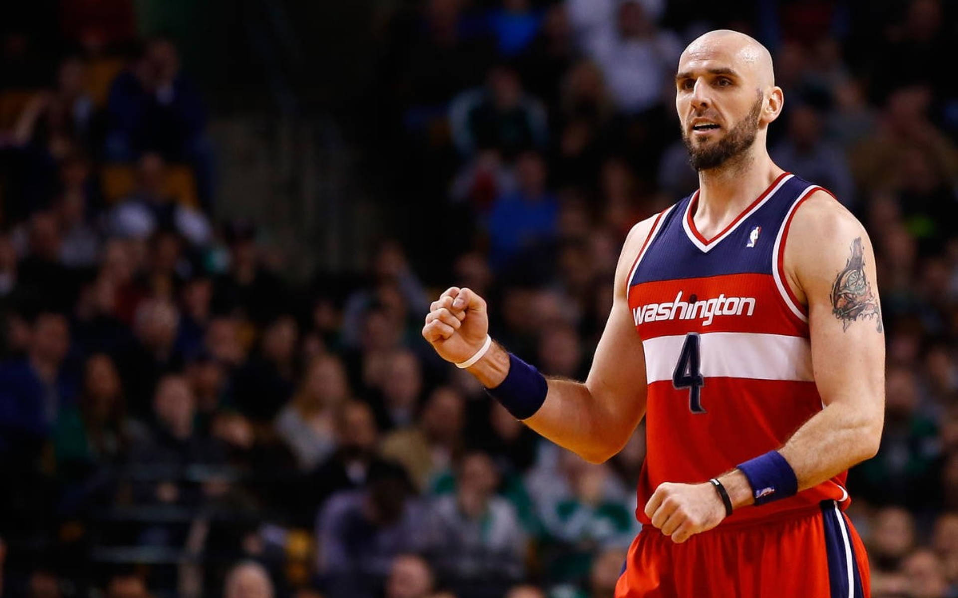 Wizards 桌布 壁紙 — 一名光頭籃球運動員身穿紅白藍華盛頓球衣，在比賽中握緊拳頭，身後是模糊的人群。