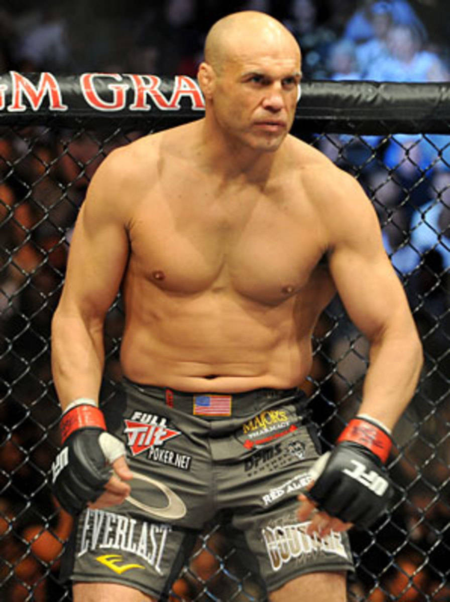 MMA 桌布 壁紙 — 一名光頭肌肉發達的戰士穿著黑色短褲和手套，在UFC八角籠內激烈地站立，背後是模糊的人群。