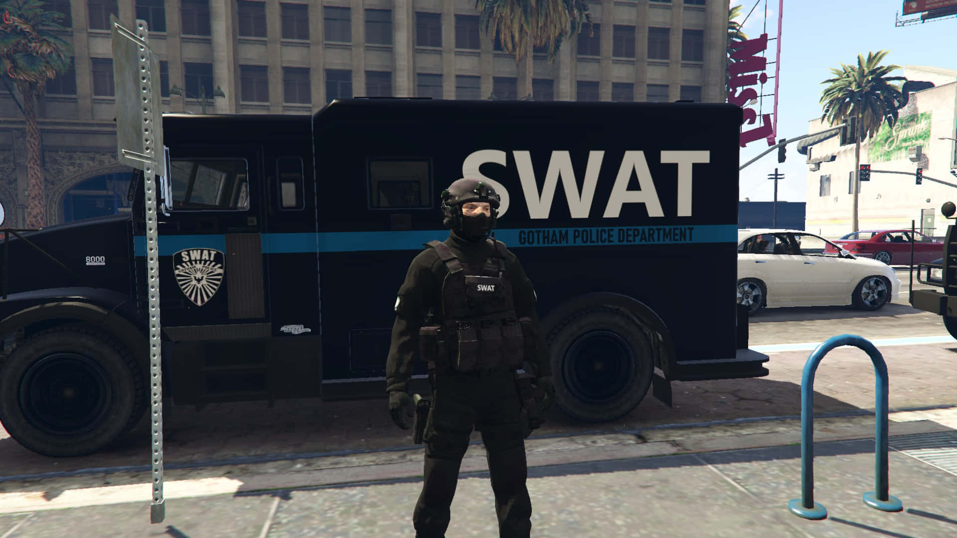 Gotham City Police Department 桌布 壁紙 — 一名全副武裝的SWAT警員在陽光明媚的城市人行道上，站在一輛標有高譚警察局的黑色SWAT卡車旁保持警覺。