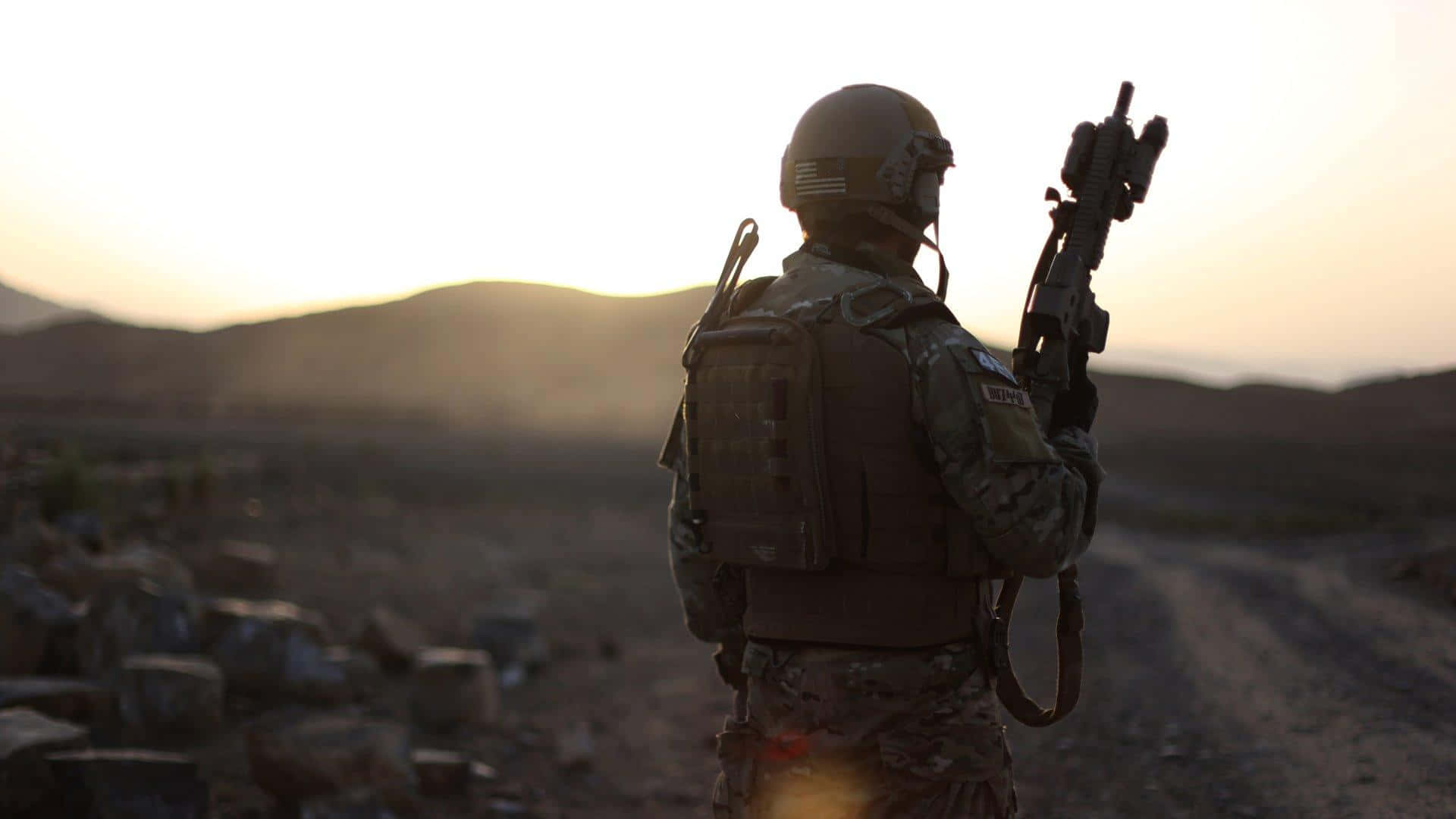 Special Forces 桌布 壁紙 — 一名全副武裝的士兵在岩石沙漠景觀上，以金色日落為背景形成剪影。