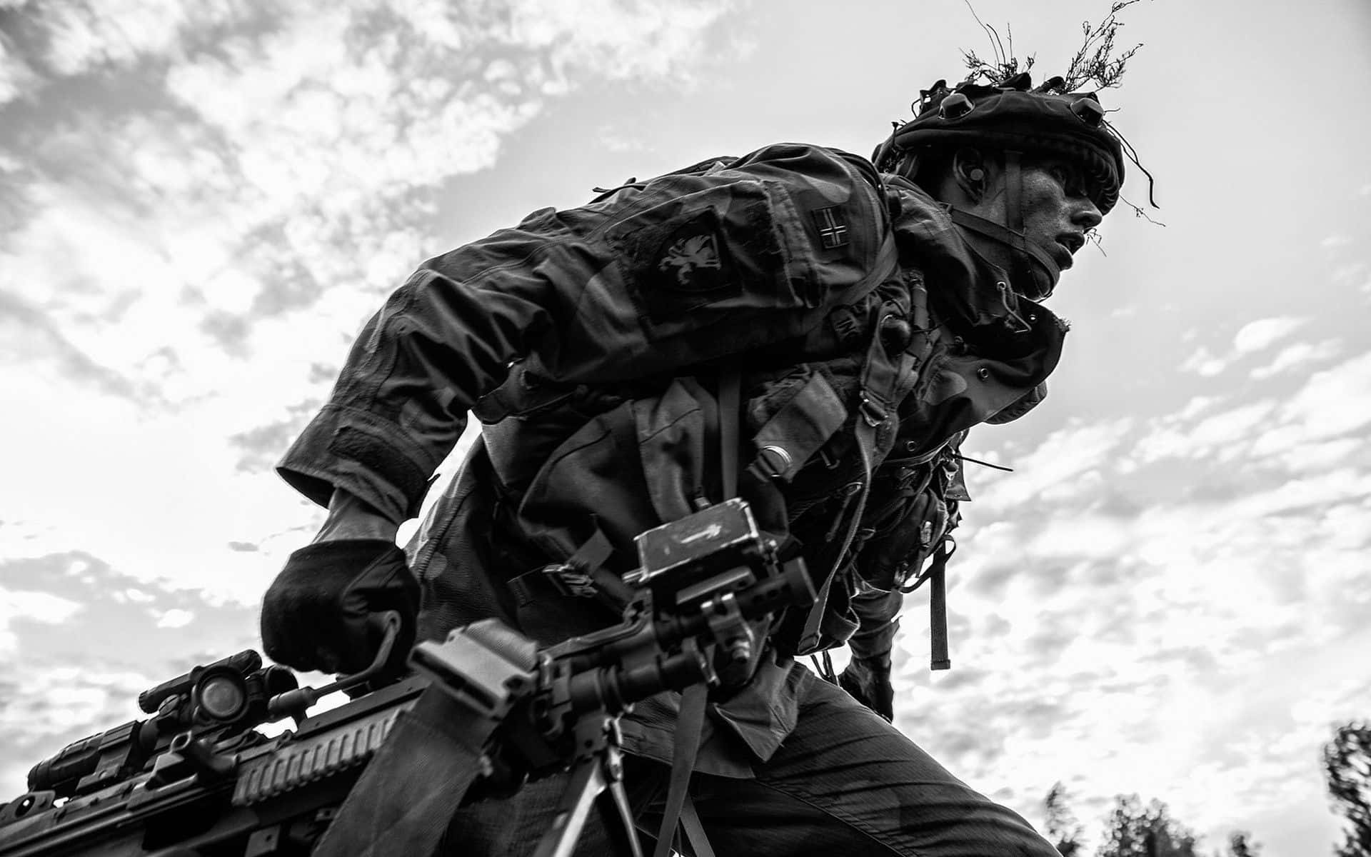軍隊 桌布 壁紙 — 一名全副武裝的士兵在陰天背景下持步槍前進，呈現粗糙的黑白照片效果。