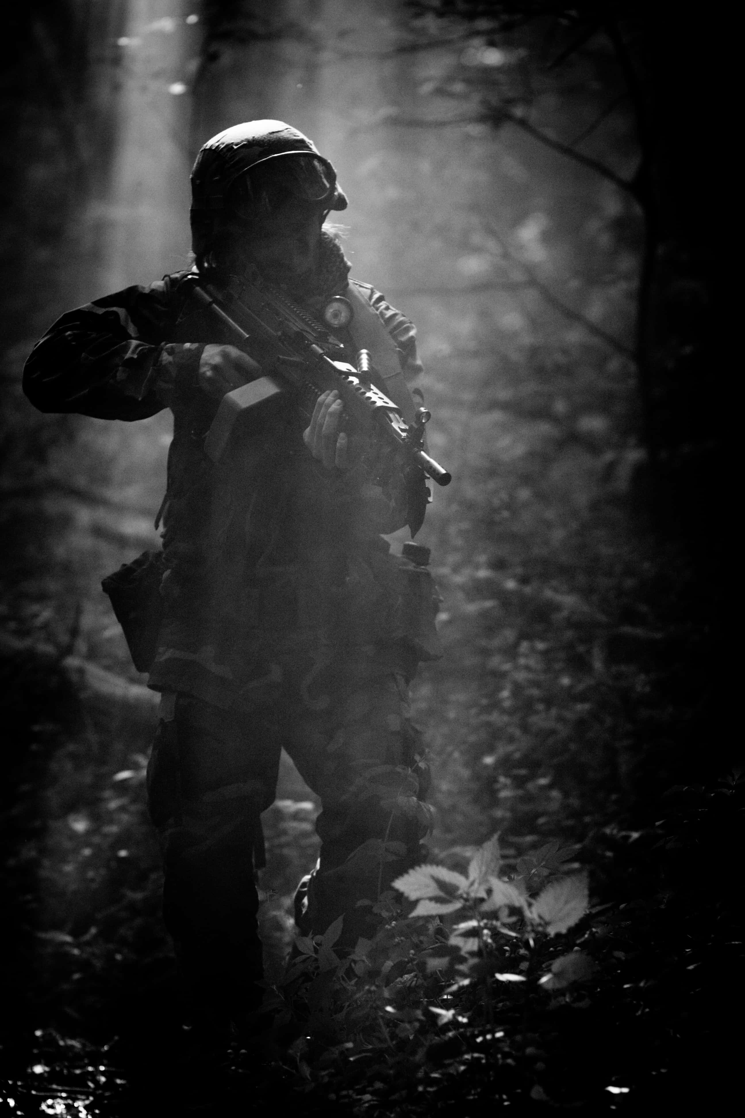 黑白 桌布 壁紙 — 一名全副武裝的士兵在霧氣瀰漫的森林中保持警覺，陽光從背後的樹木間穿透而過。