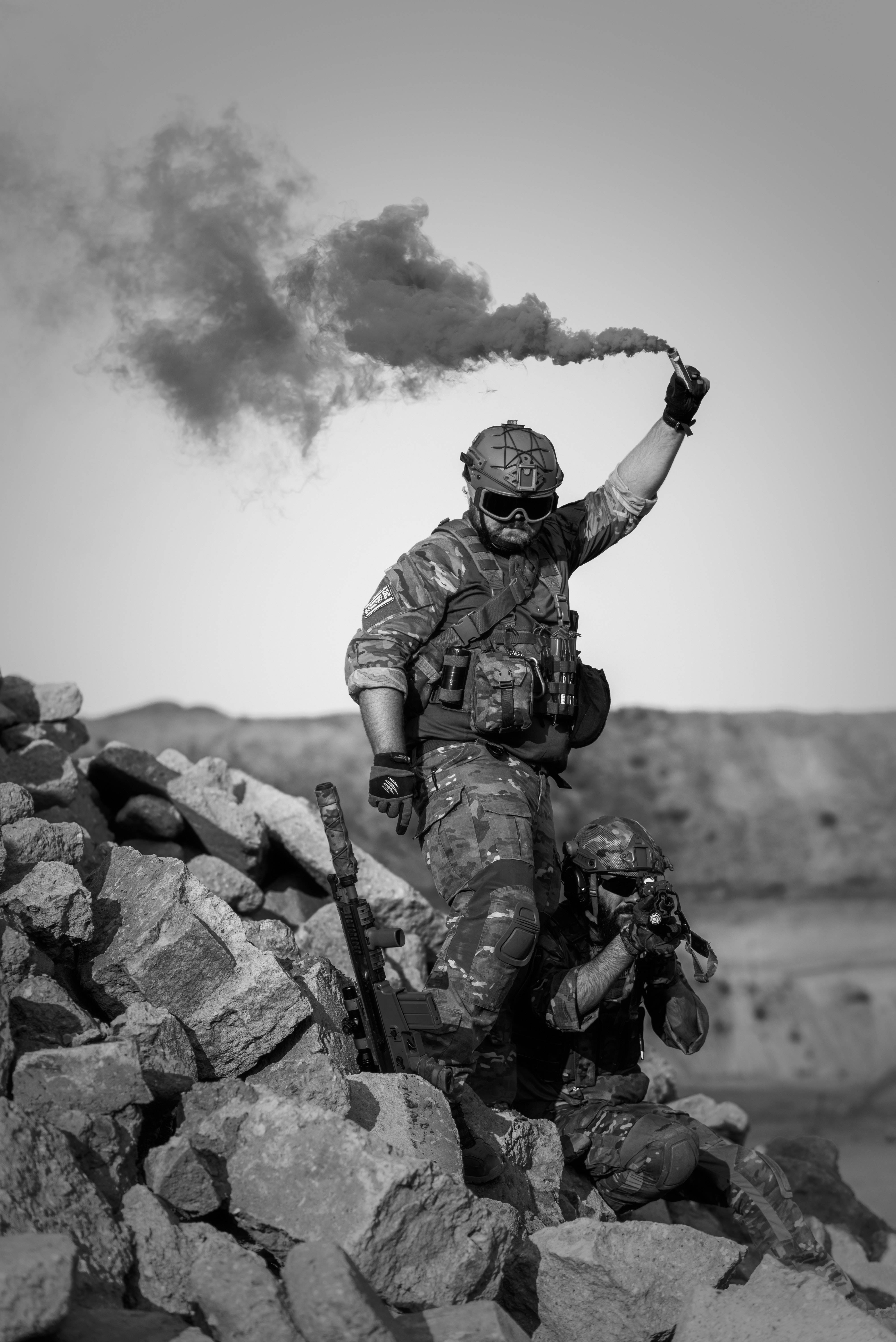 Danger 桌布 壁紙 — 一名全副武裝的士兵從信號彈中釋放煙霧，而另一名士兵蹲在瓦礫後面，形成鮮明的黑白場景。