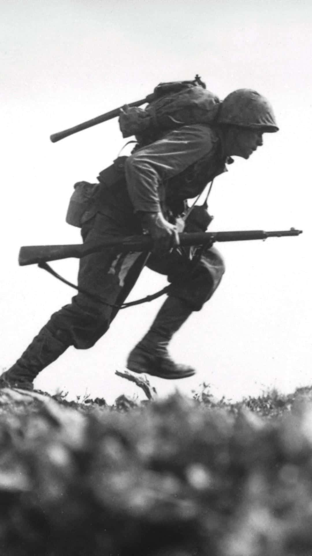 Ww2 iPhone 桌布 壁紙 — 一名全副武裝的士兵手持步槍，在嚴峻的多雲天空下衝上山坡。