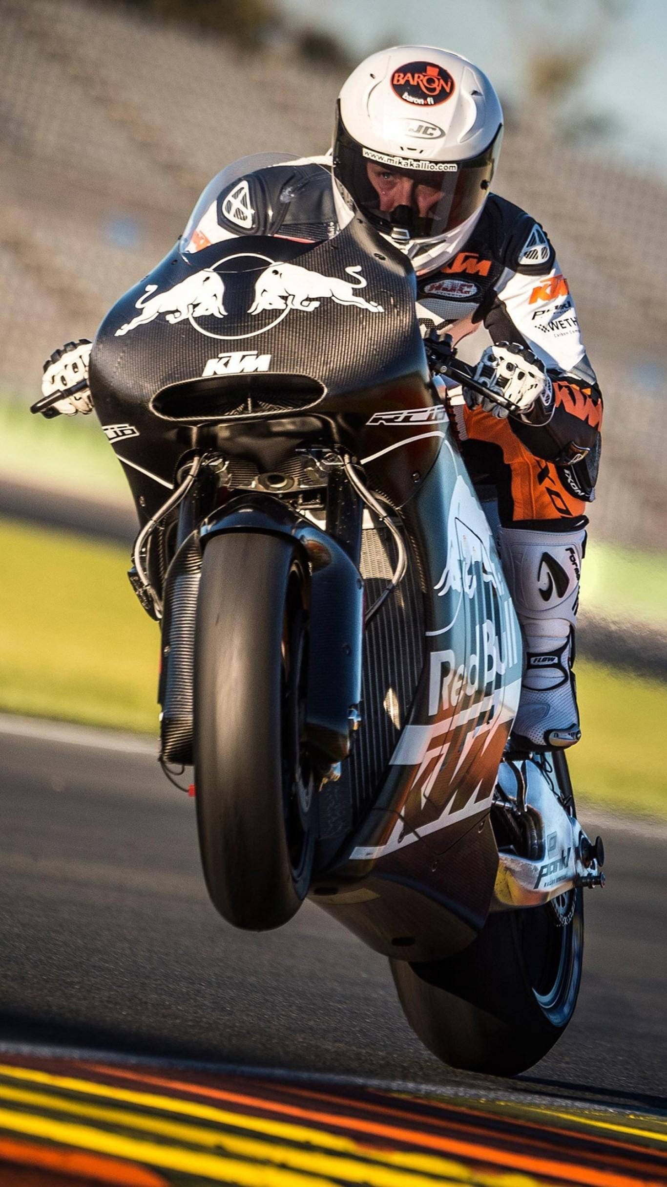 Racing 桌布 壁紙 — 一名全副裝備的摩托車手在賽道上騎著KTM賽車，前輪抬起，傾斜入彎。
