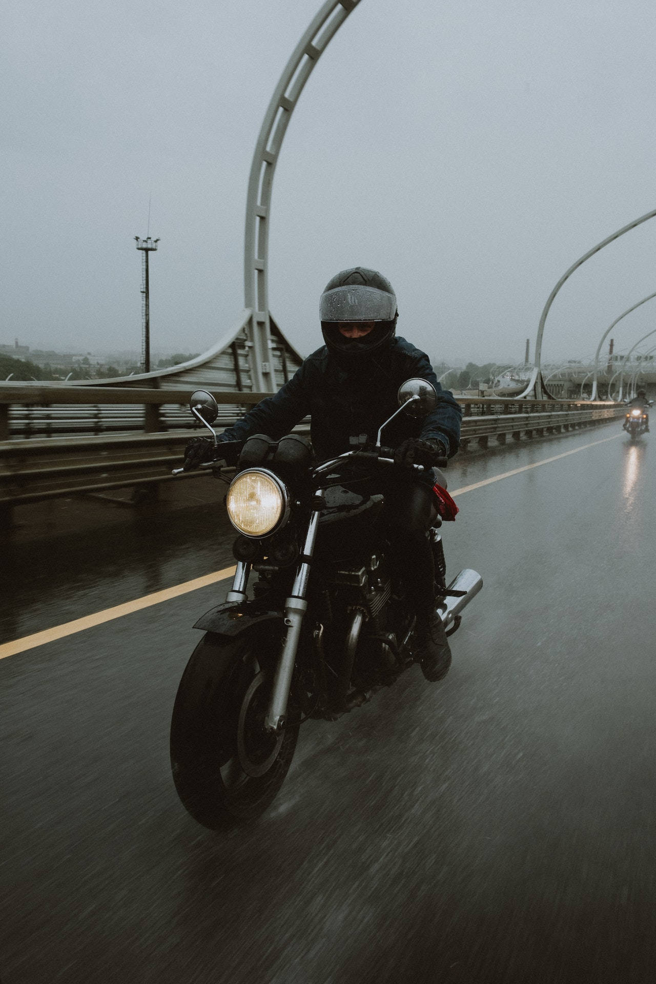Road 桌布 壁紙 — 一名全副裝備的摩托車手在雨天騎著經典摩托車，在彎曲的橋下行駛，畫面帶有模糊的動感。
