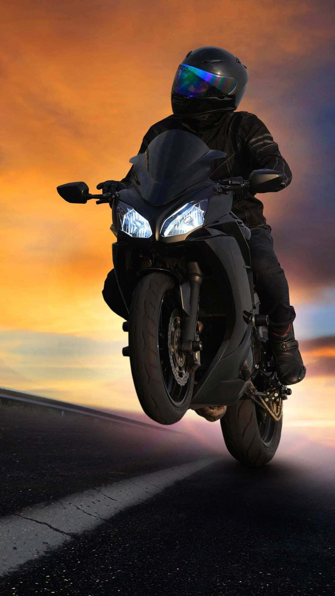  壁紙 — 一名全副裝備的機車手在黑色跑車上表演前輪離地，背景是火紅的日落天空。