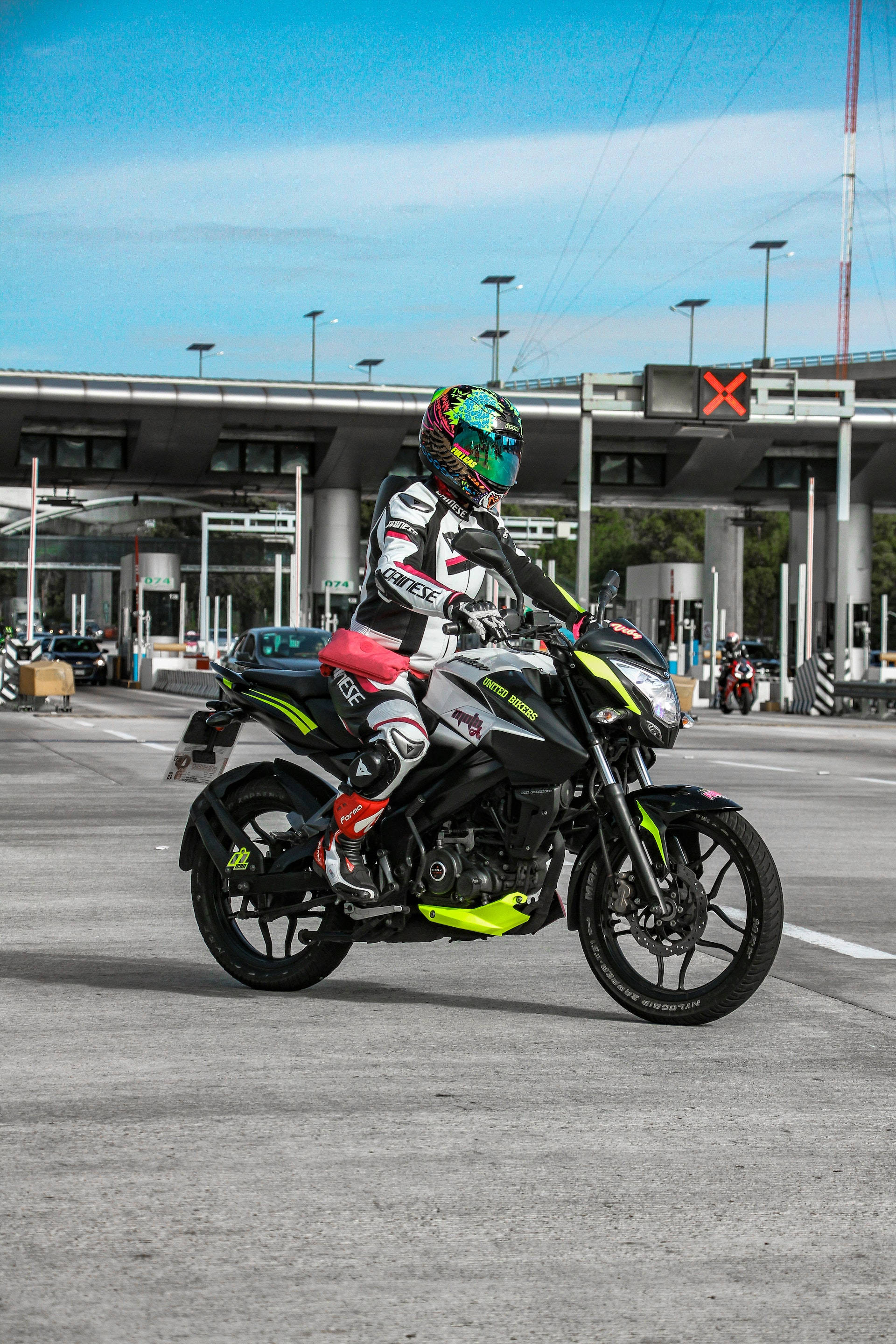 Racing 桌布 壁紙 — 一名全副裝備的機車騎士在晴朗的藍天下，於高速公路收費站騎著一輛運動型黑色和螢光綠色的機車。