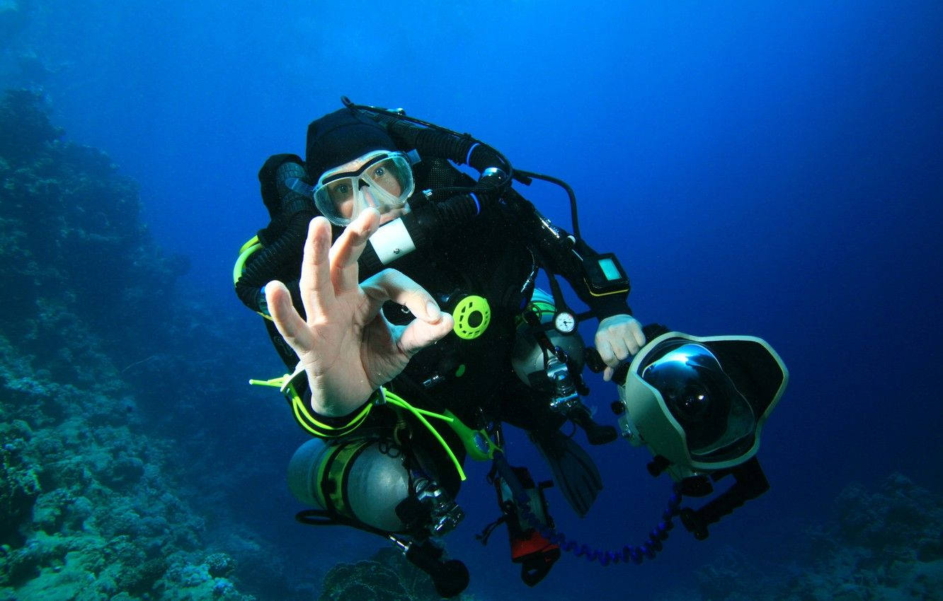 Snorkeling 桌布 壁紙 — 一名全副裝備的水肺潛水員在深藍色海洋的珊瑚礁附近水下做出OK手勢。