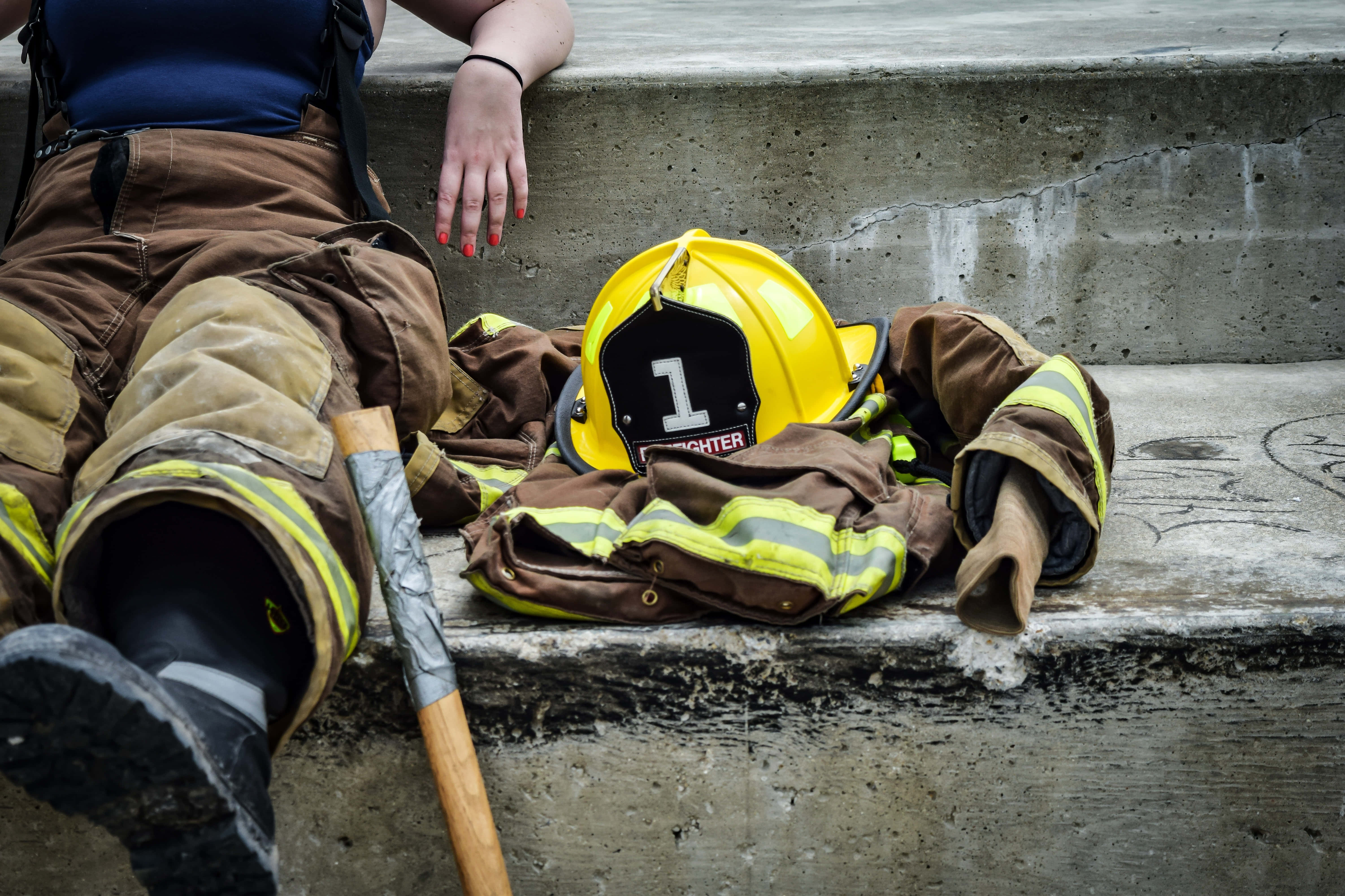 Fireman 桌布 壁紙 — 一名全副裝備的消防員在接到任務後，在黃色頭盔和斧頭旁邊的混凝土台階上休息。