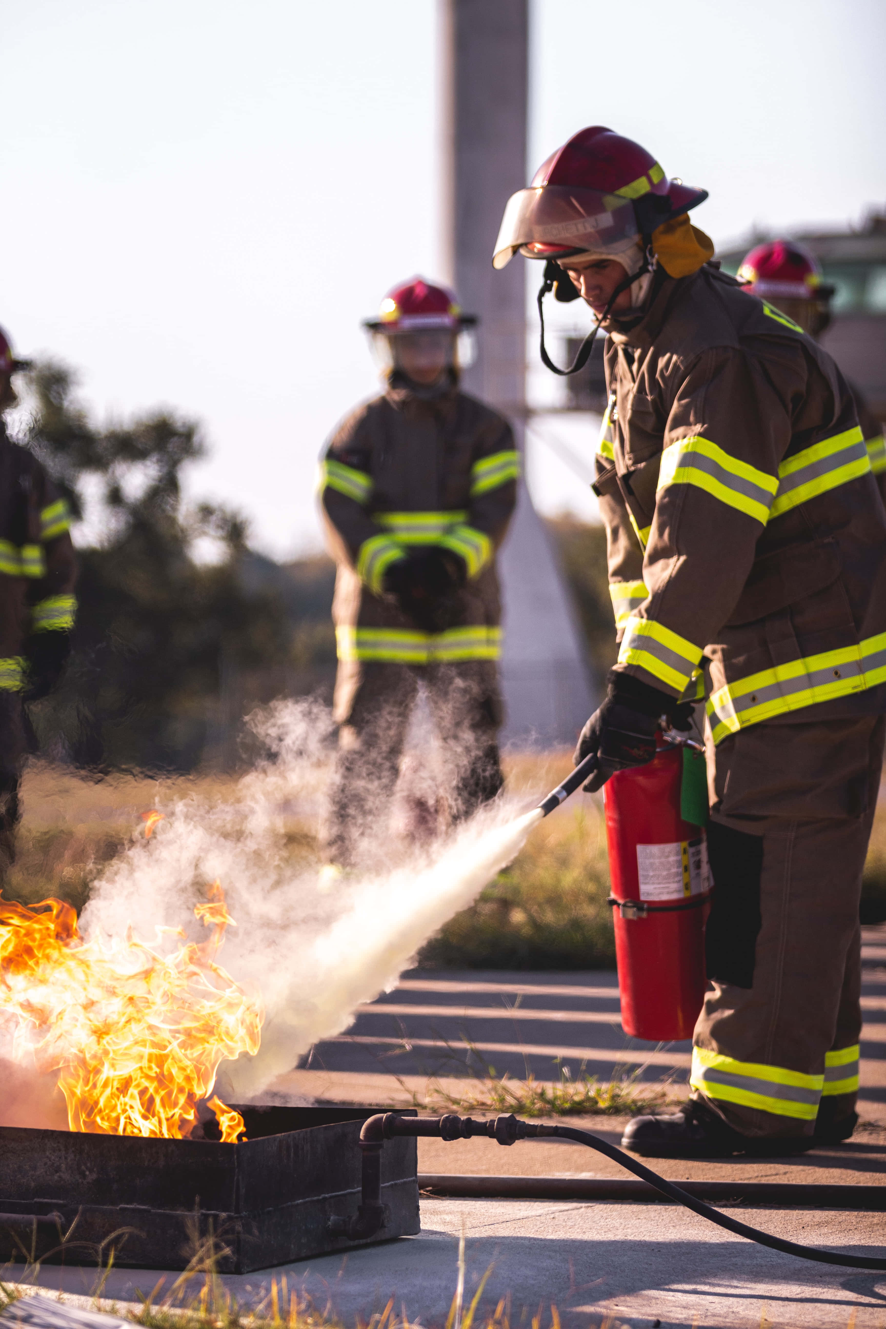 消防員 桌布 壁紙 — 一名全副裝備的消防員在訓練期間使用紅色滅火器撲滅金屬容器內受控的火災。
