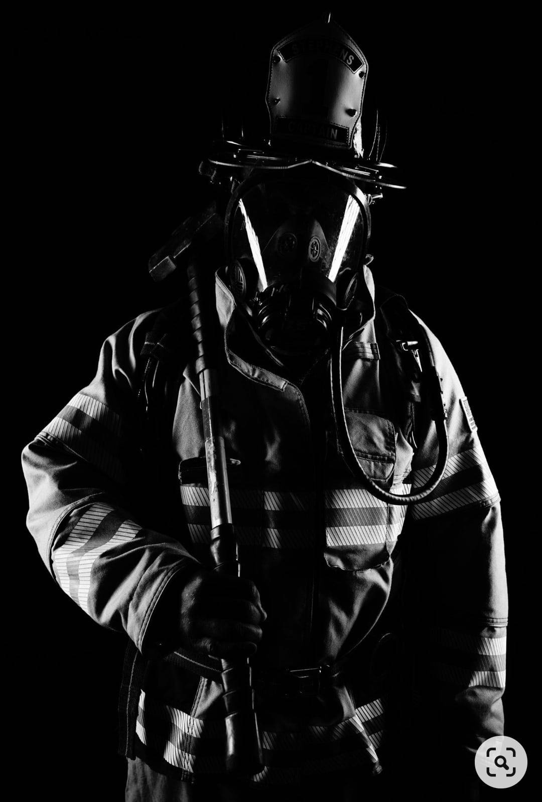 Firefighter 桌布 壁紙 — 一名全副裝備的消防員站在黑色背景前，手持斧頭，在戲劇性燈光下呈現剪影效果。