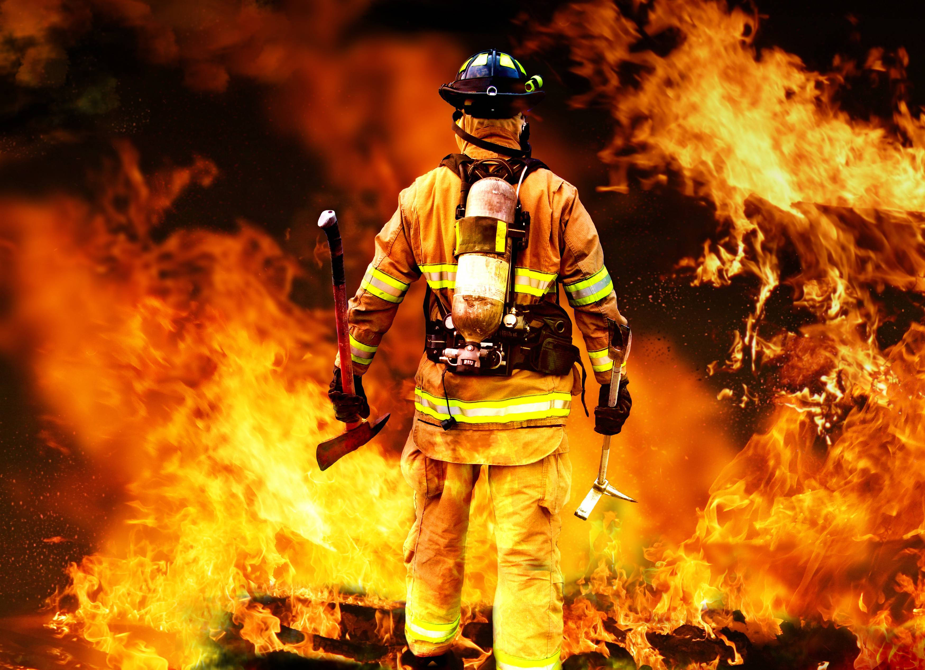 Firefighter 桌布 壁紙 — 一名全副裝備的消防員背向鏡頭，手持斧頭面對熊熊烈火。