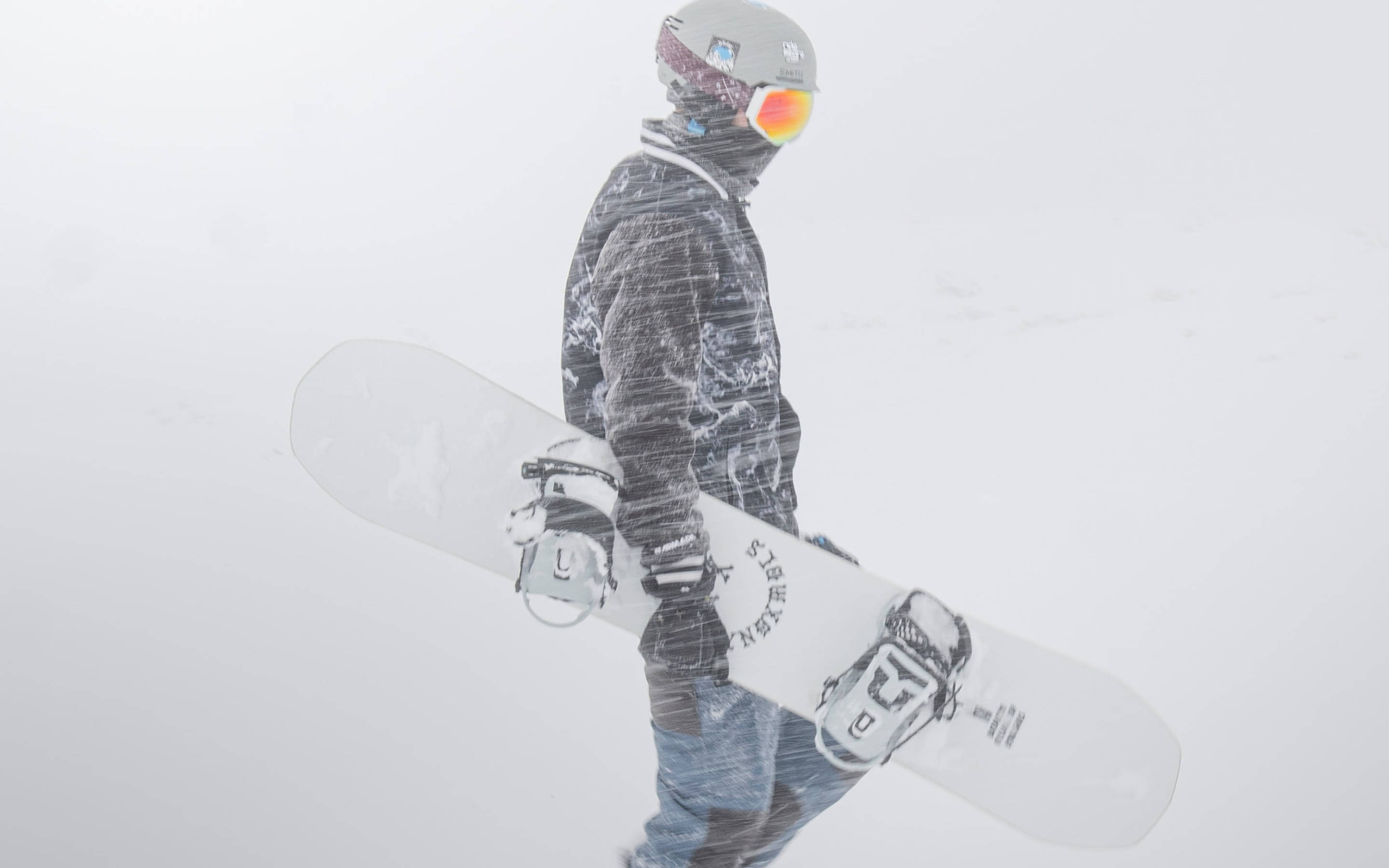 Snowboarding 桌布 壁紙 — 一名全副裝備的滑雪板手拿著白色滑雪板在暴風雪中行走。