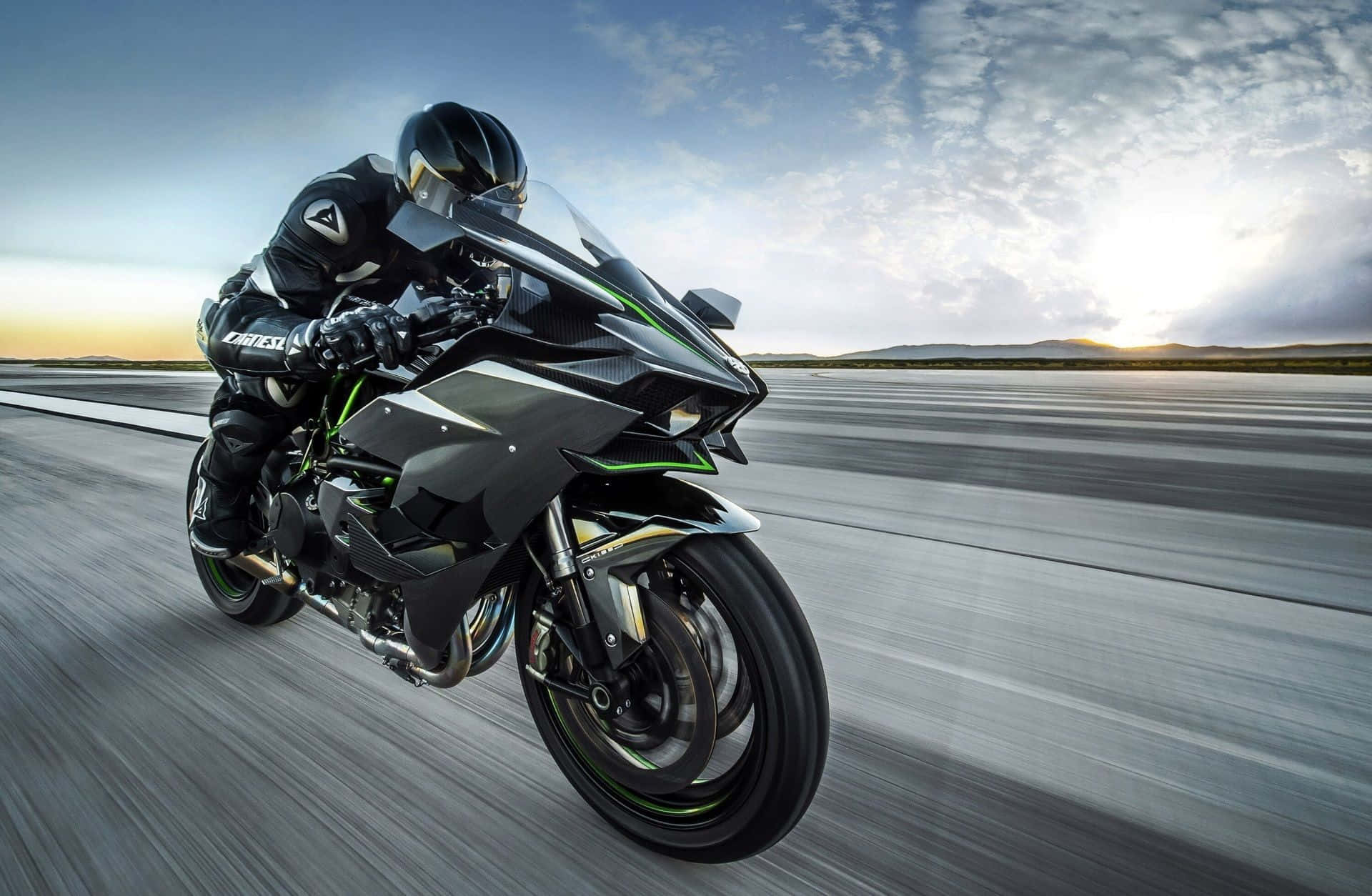 Kawasaki Desktop 桌布 壁紙 — 一名全副裝備的騎士在日落時分，在沙漠公路上高速馳騁的流線型黑綠色運動機車上傾身入彎。