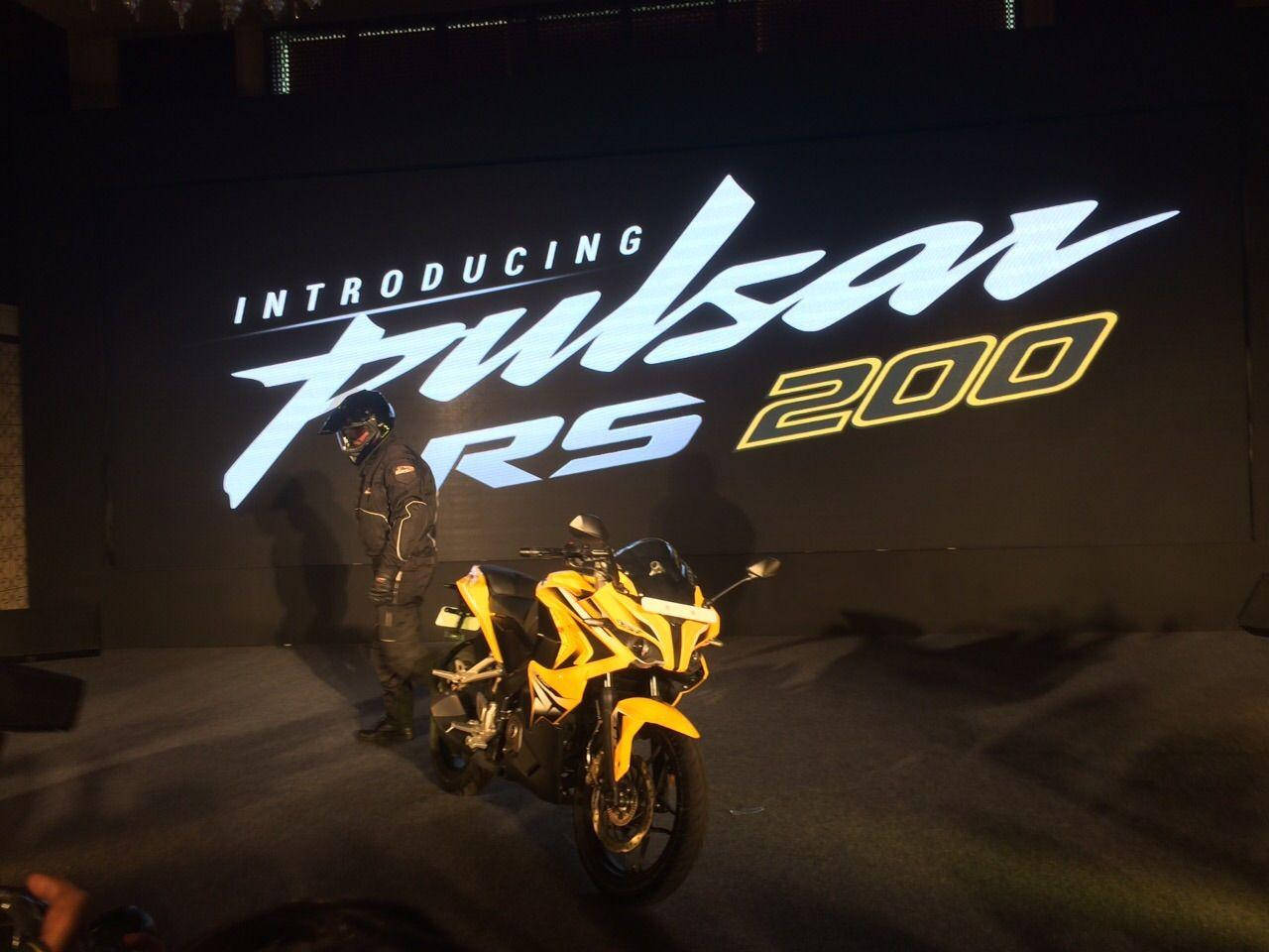 Racing 桌布 壁紙 — 一名全副裝備的騎士站在一輛亮黃色Pulsar RS 200機車旁，上方是一個大型發光的發射螢幕。