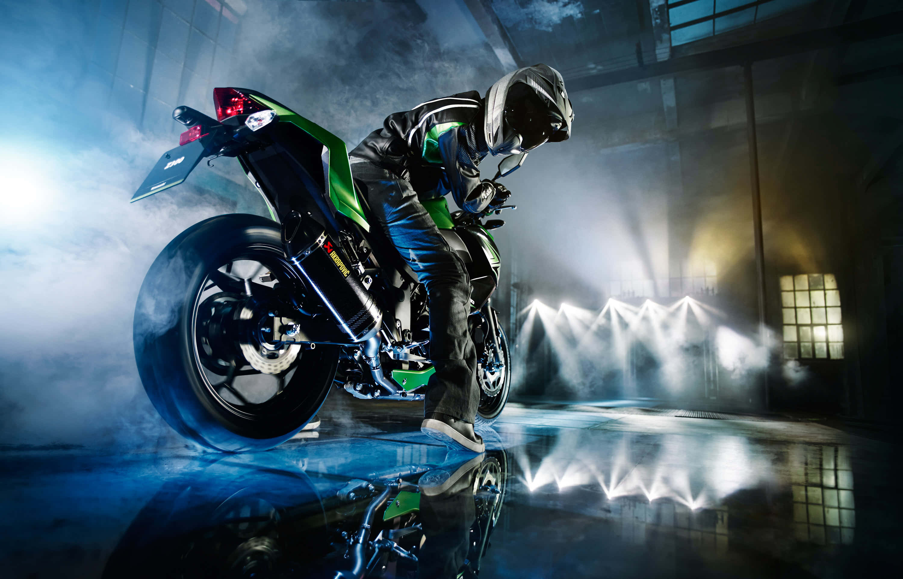 Superbike 桌布 壁紙 — 一名全副裝備的騎士靠在一輛綠色和黑色的運動摩托車上，身處煙霧瀰漫的工業倉庫，被戲劇性的聚光燈照亮。