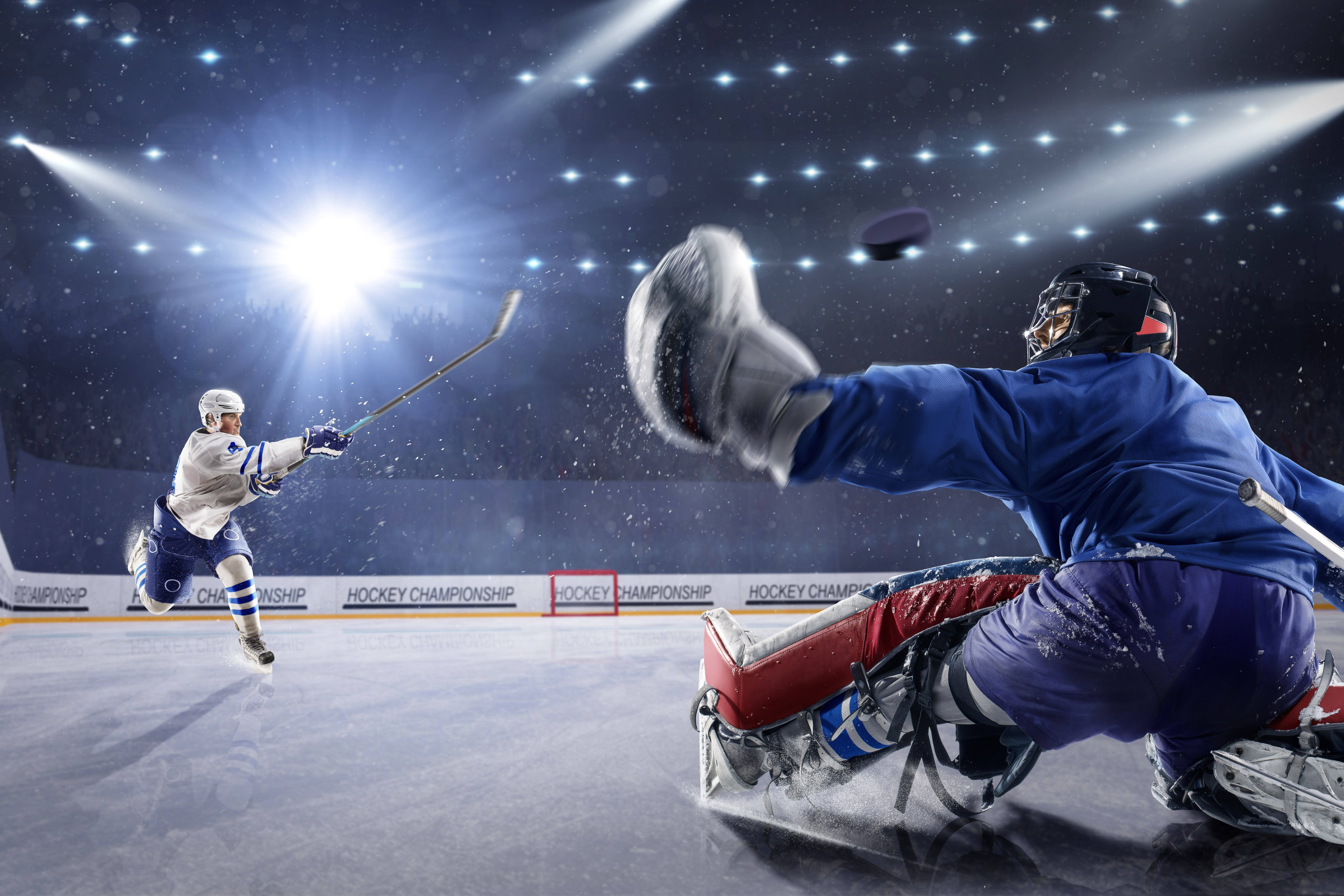 hockey 桌布 壁紙 — 一名冰球運動員在明亮的場館燈光下射門，守門員飛身撲救試圖阻擋。