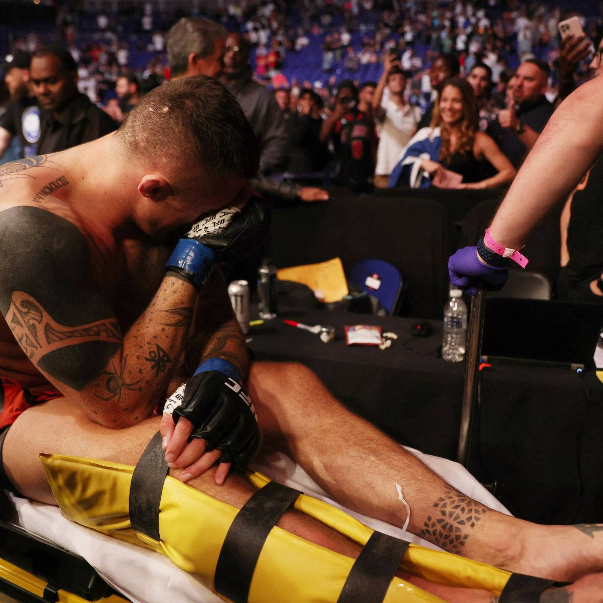 UFC 桌布 壁紙 — 一名刺青戰士戴著黑色手套，在殘酷的MMA比賽後低頭坐在擔架上，顯得沮喪。