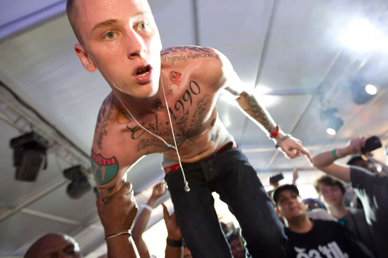 mgk 桌布 壁紙 — 一名刺青男子在明亮的舞台燈光下被人群舉起於演唱會中。