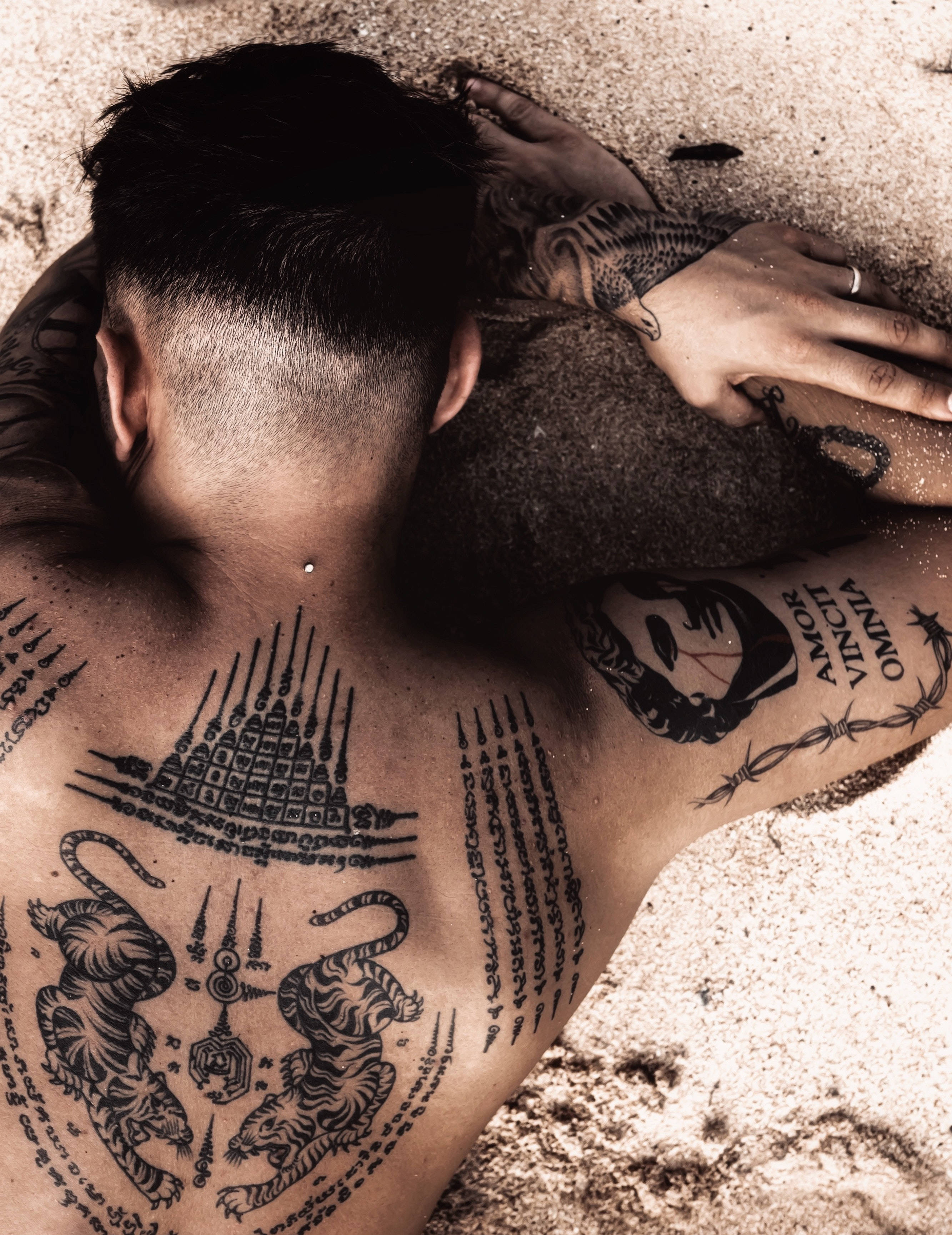 Tattoo 桌布 壁紙 — 一名刺青男子躺在沙地上，複雜的黑色墨水圖案覆蓋他的背部和手臂。