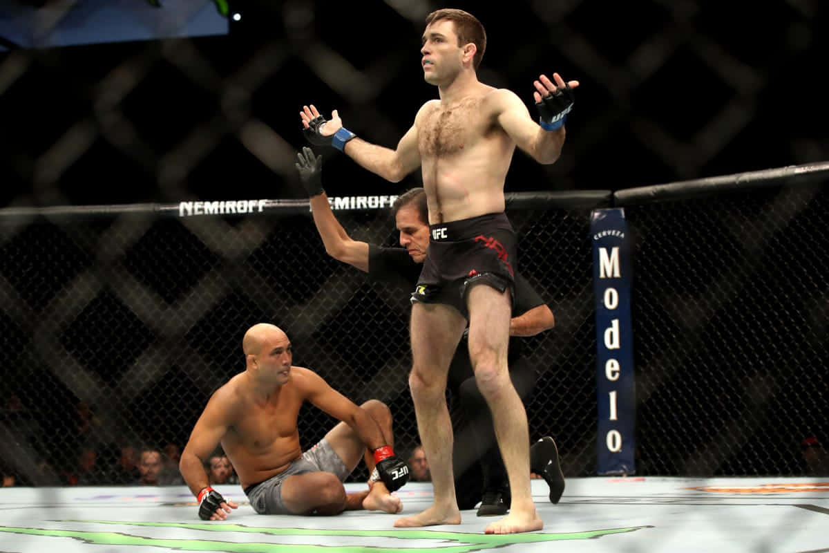 UFC 桌布 壁紙 — 一名勝利的MMA拳手在八角籠中凱旋，而他的對手則坐在墊子上失敗。