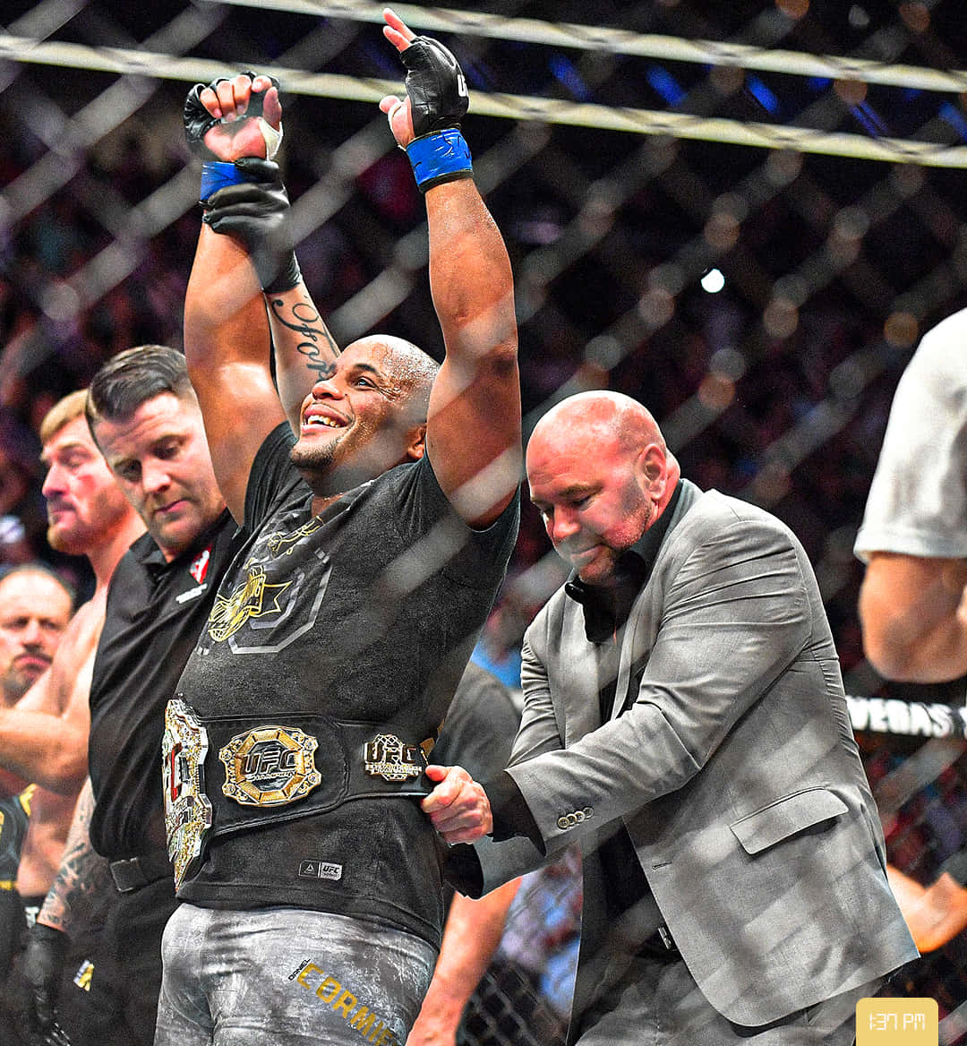 MMA 桌布 壁紙 — 一名勝利的UFC拳手在八角籠內高舉雙臂慶祝，裁判將冠軍腰帶繫在他腰間。