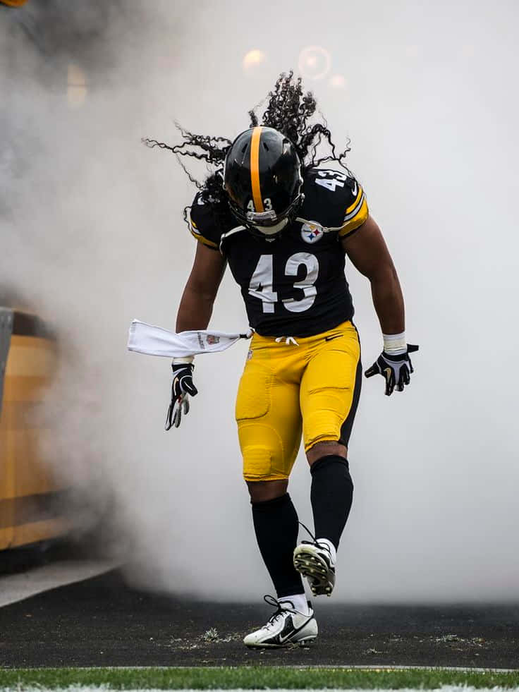 Troy Polamalu 桌布 壁紙 — 一名匹茲堡鋼人隊美式足球員身穿黑黃色球衣，在煙霧中走過草地和背景有體育場燈光的球場。