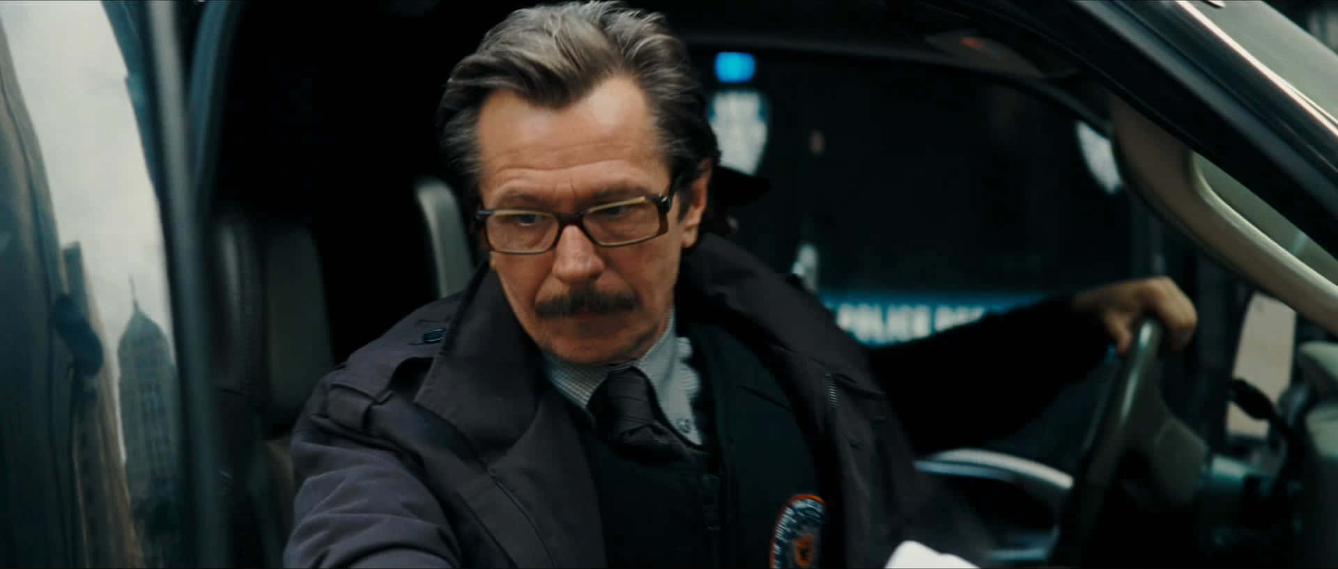 Commissioner Gordon 桌布 壁紙 — 一名嚴肅的警察戴著眼鏡和鬍子坐在巡邏車內，專注地向前看。