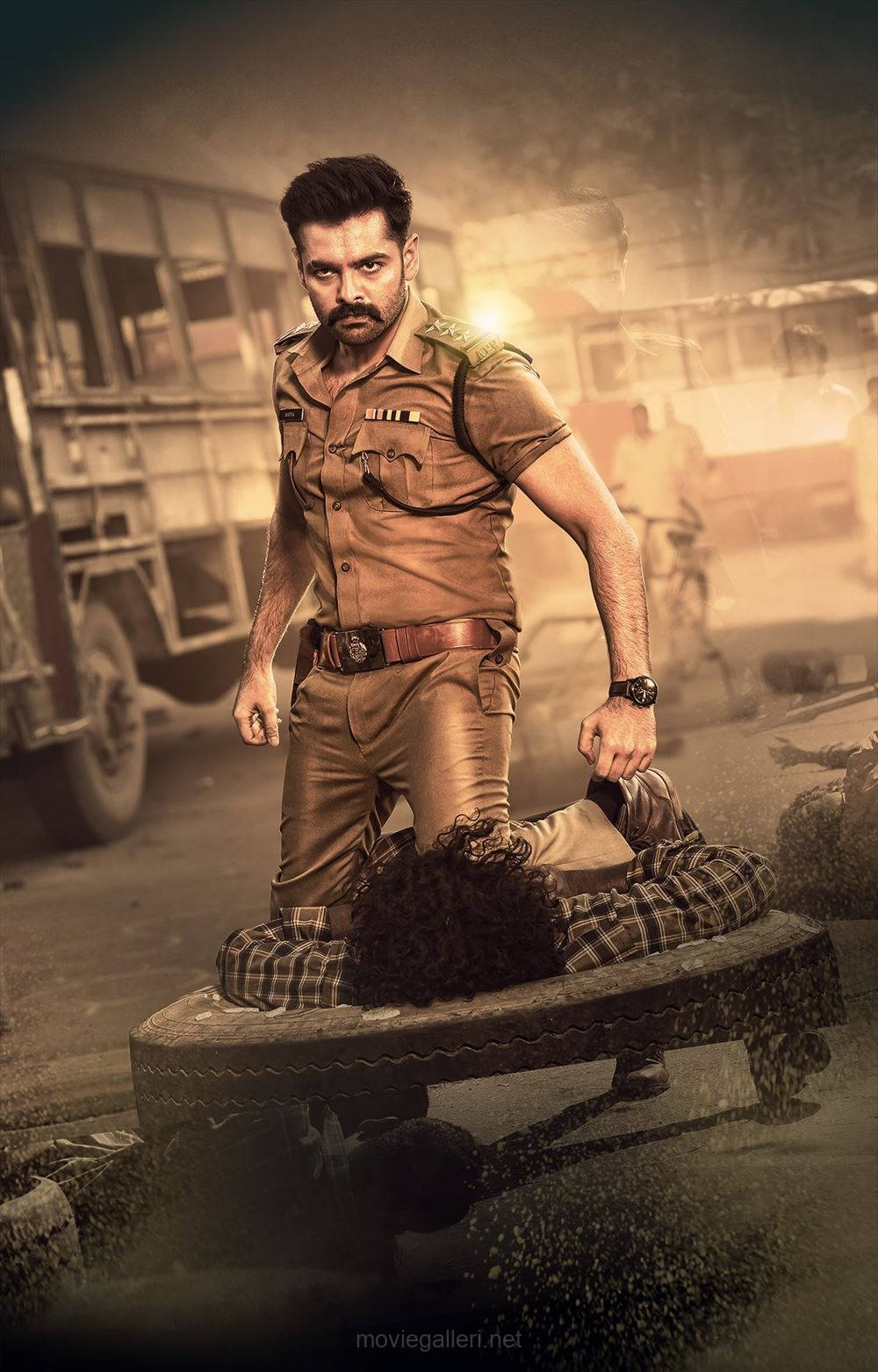 Ram Pothineni 桌布 壁紙 — 一名嚴肅的警察穿著卡其色制服，站在一個被制服的男人上方，該男人坐在一條塵土飛揚的城市街道上的木長椅上。