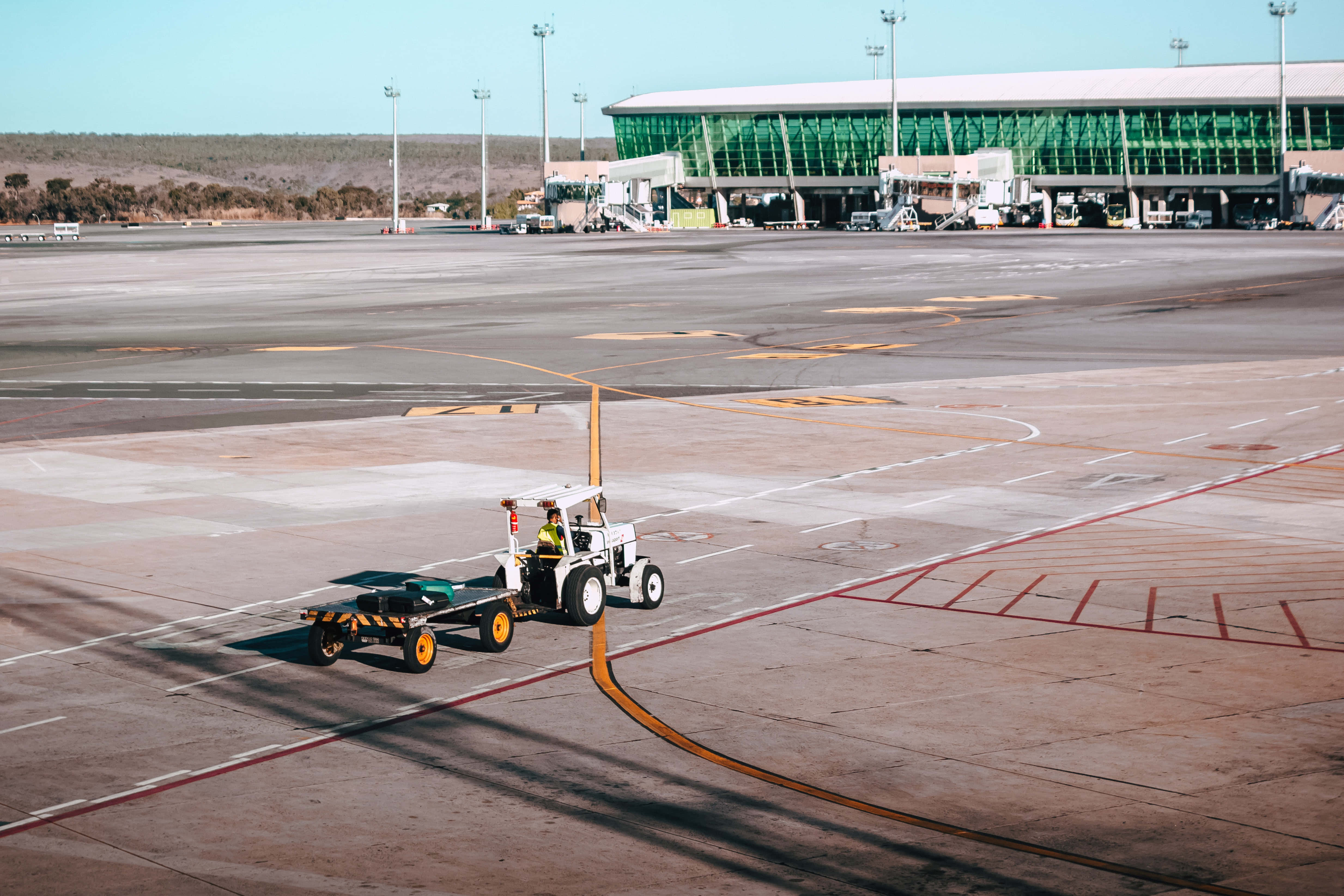 Airport 桌布 壁紙 — 一名地勤人員在陽光普照的機場停機坪上操作牽引車，拖動一條登機橋，靠近一個現代化航廈。