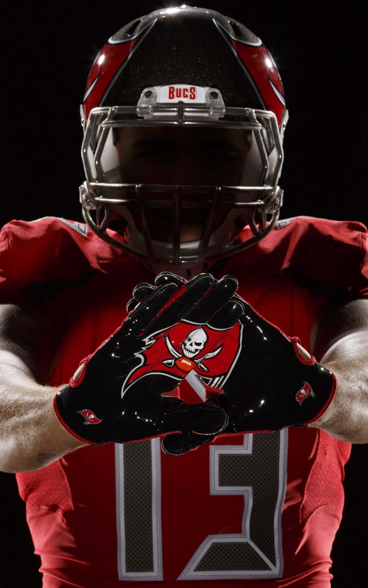 Mike Evans 桌布 壁紙 — 一名坦帕灣海盜隊美式足球員身穿紅色裝備，在黑色背景前將美式足球放在頭盔下。