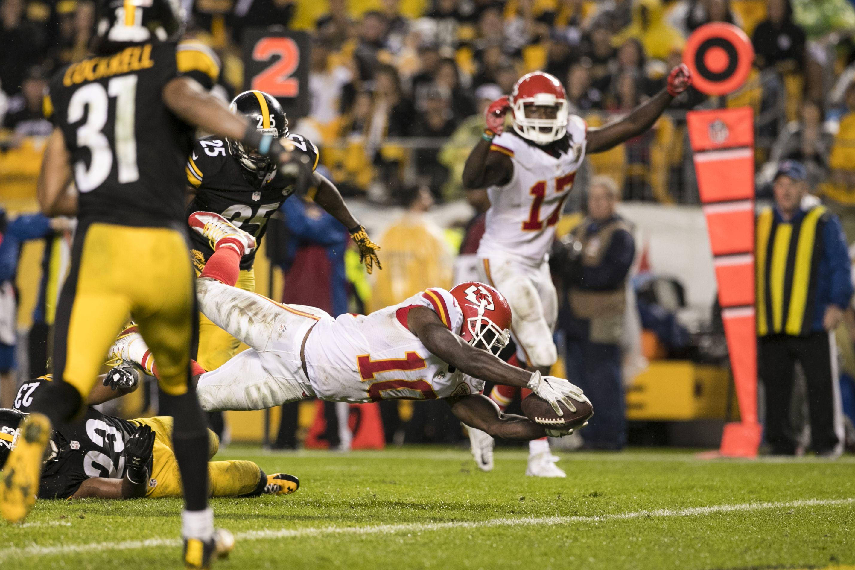 Tyreek Hill 桌布 壁紙 — 一名堪薩斯城酋長隊球員在夜間美式足球比賽中飛身達陣，匹茲堡鋼人隊防守球員逼近。