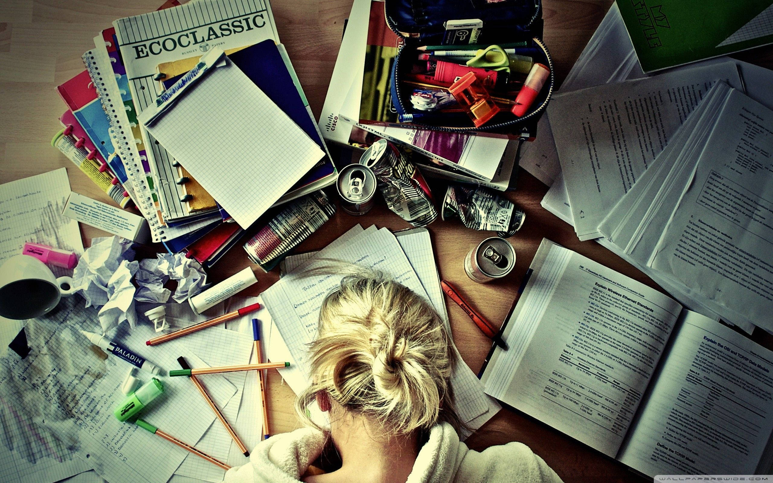 Studying 桌布 壁紙 — 一名壓力大的學生，金髮紮成髮髻，將頭靠在堆滿紙張、教科書、筆和汽水罐的凌亂木桌上。