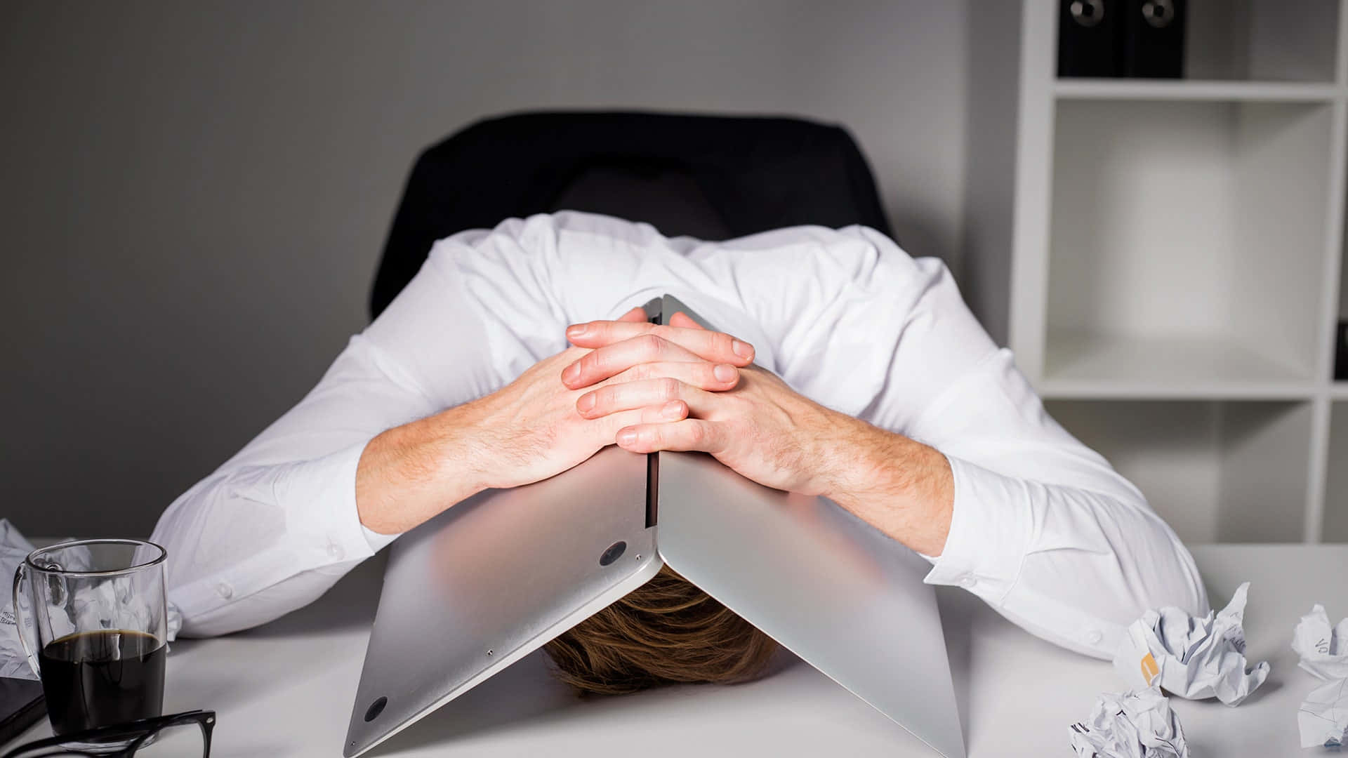 stressed 桌布 壁紙 — 一名壓力大的辦公室職員將頭靠在被皺巴巴的紙張和咖啡杯包圍的筆記型電腦鍵盤上。