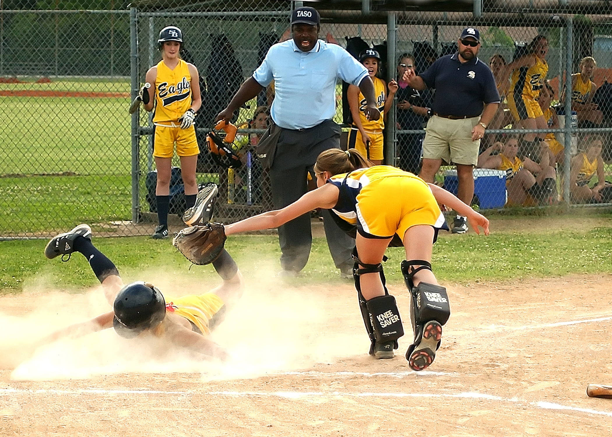 Softball 桌布 壁紙 — 一名壘球運動員頭部滑進本壘，捕手在塵土飛揚中飛身用手套試圖觸殺她。