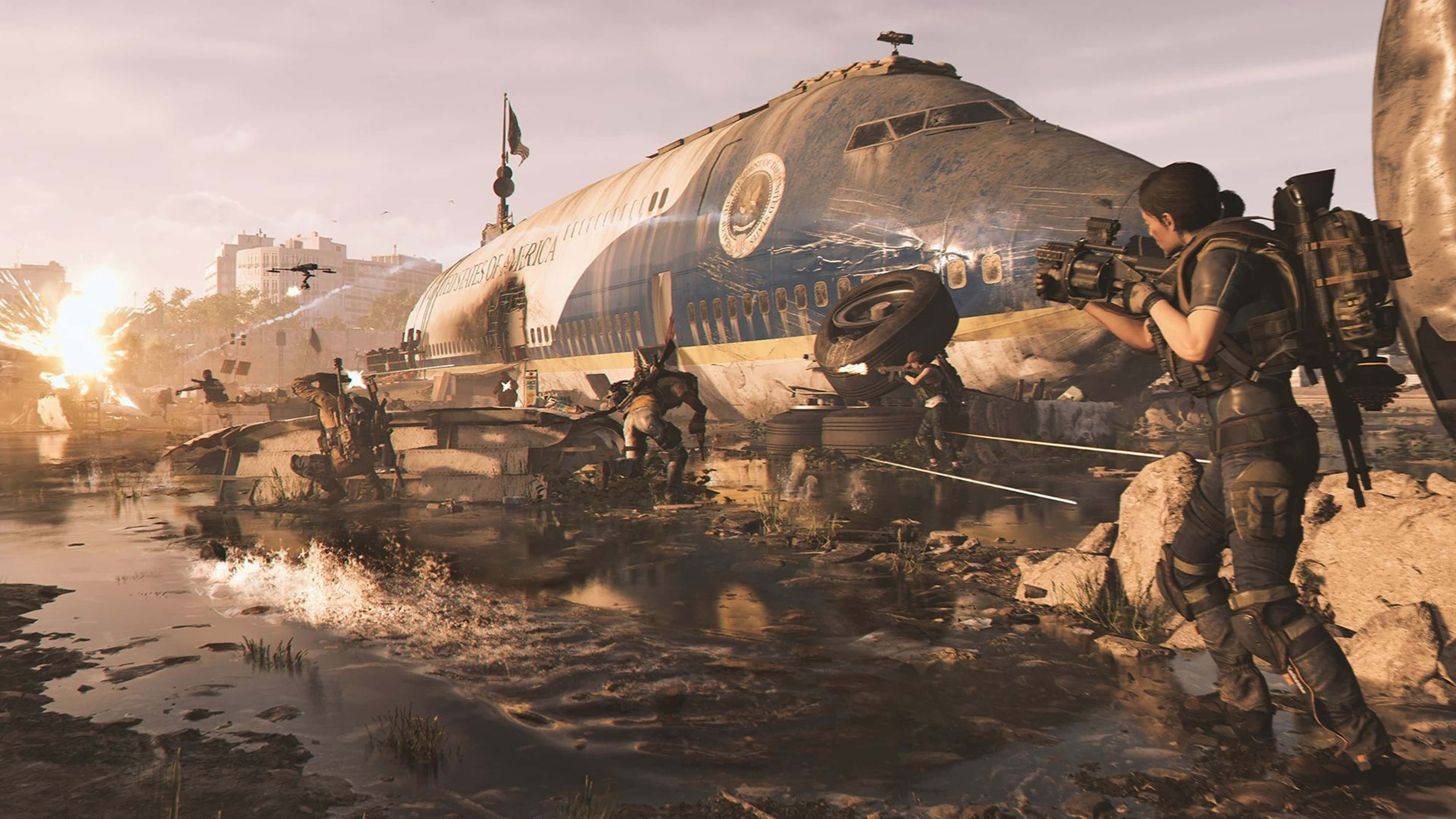 The Division 2 4K 桌布 壁紙 — 一名士兵在泥濘的戰場上開步槍射擊，背景中一架墜毀的飛機在熾熱的日落時分翻倒。