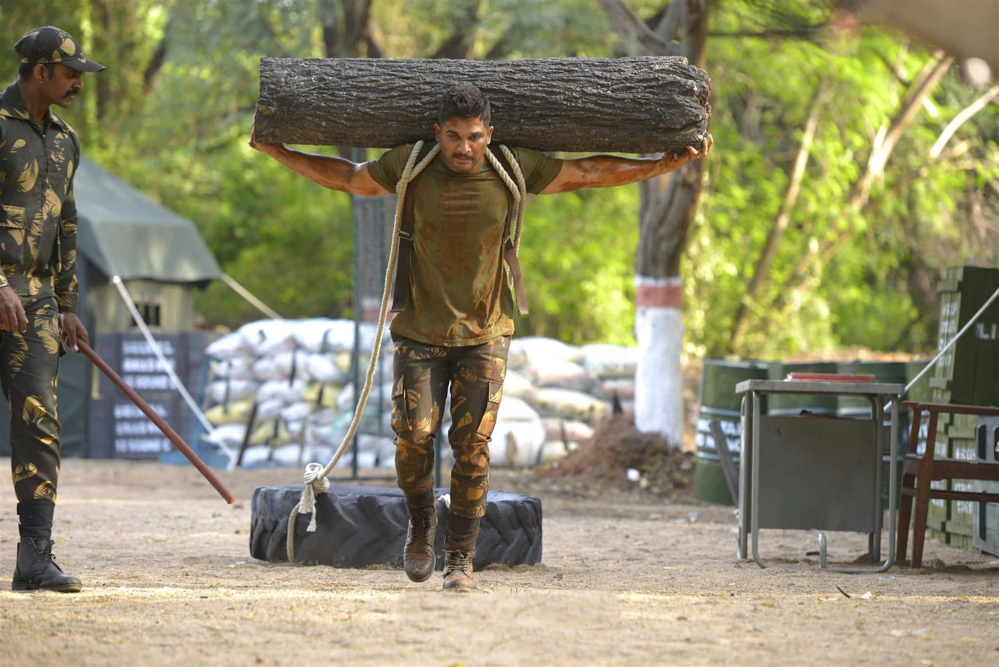 soldier 桌布 壁紙 — 一名士兵在泥濘的戶外訓練場上扛著沉重的圓木行走，另一名士兵在旁觀看。