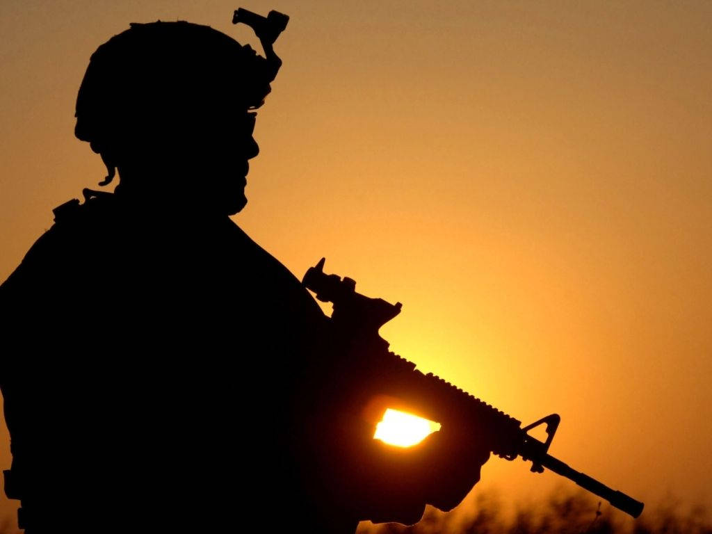 軍隊 桌布 壁紙 — 一名士兵手持步槍，映襯著發光的日落天空的剪影。
