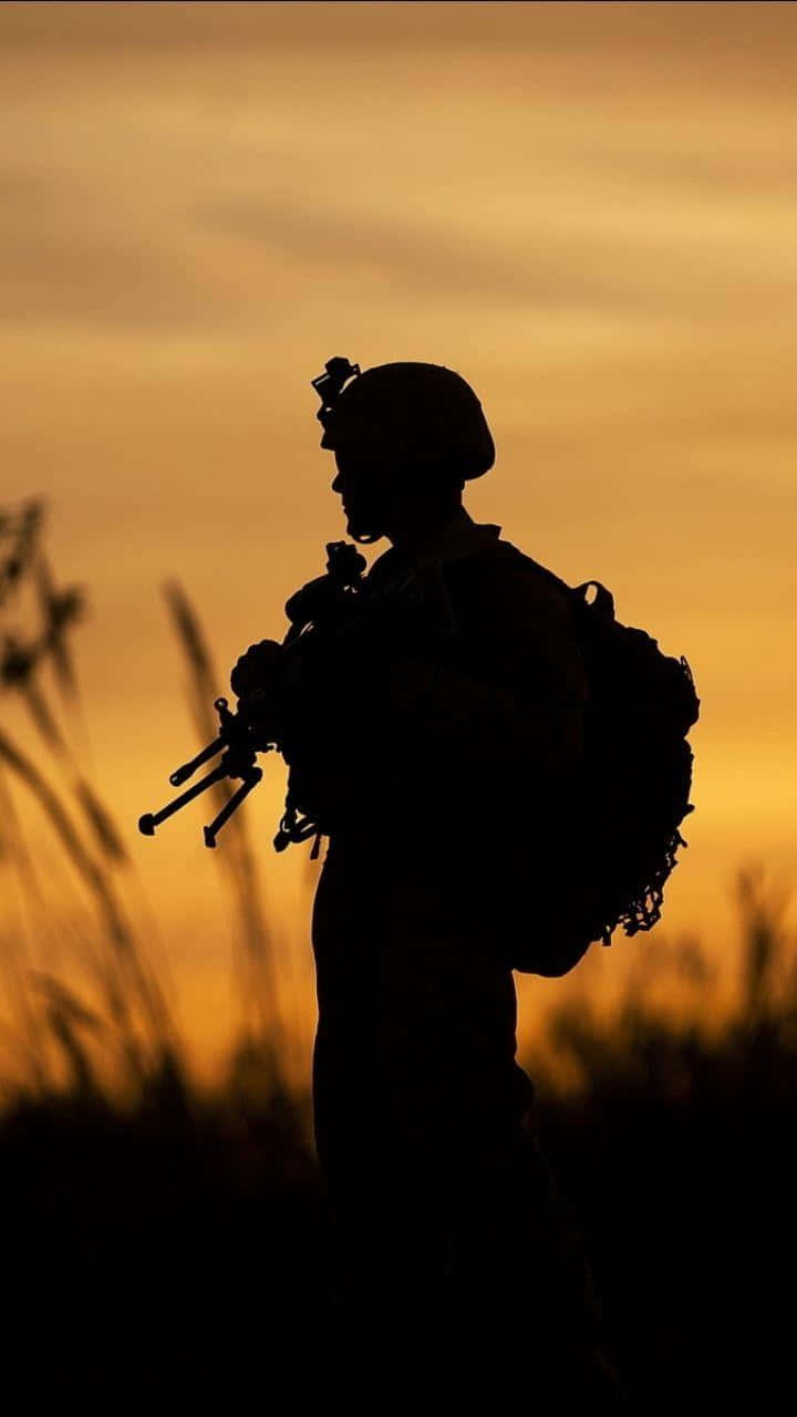 軍事動圖 桌布 壁紙 — 一名士兵手持步槍的剪影，背景是溫暖的金色日落天空，前景有模糊的草地。