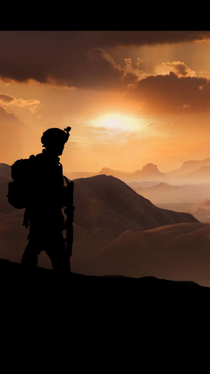 印度軍隊 桌布 壁紙 — 一名士兵的剪影站在山脊上，夕陽西下，俯瞰層層疊疊沐浴在金色光芒中的山峰。