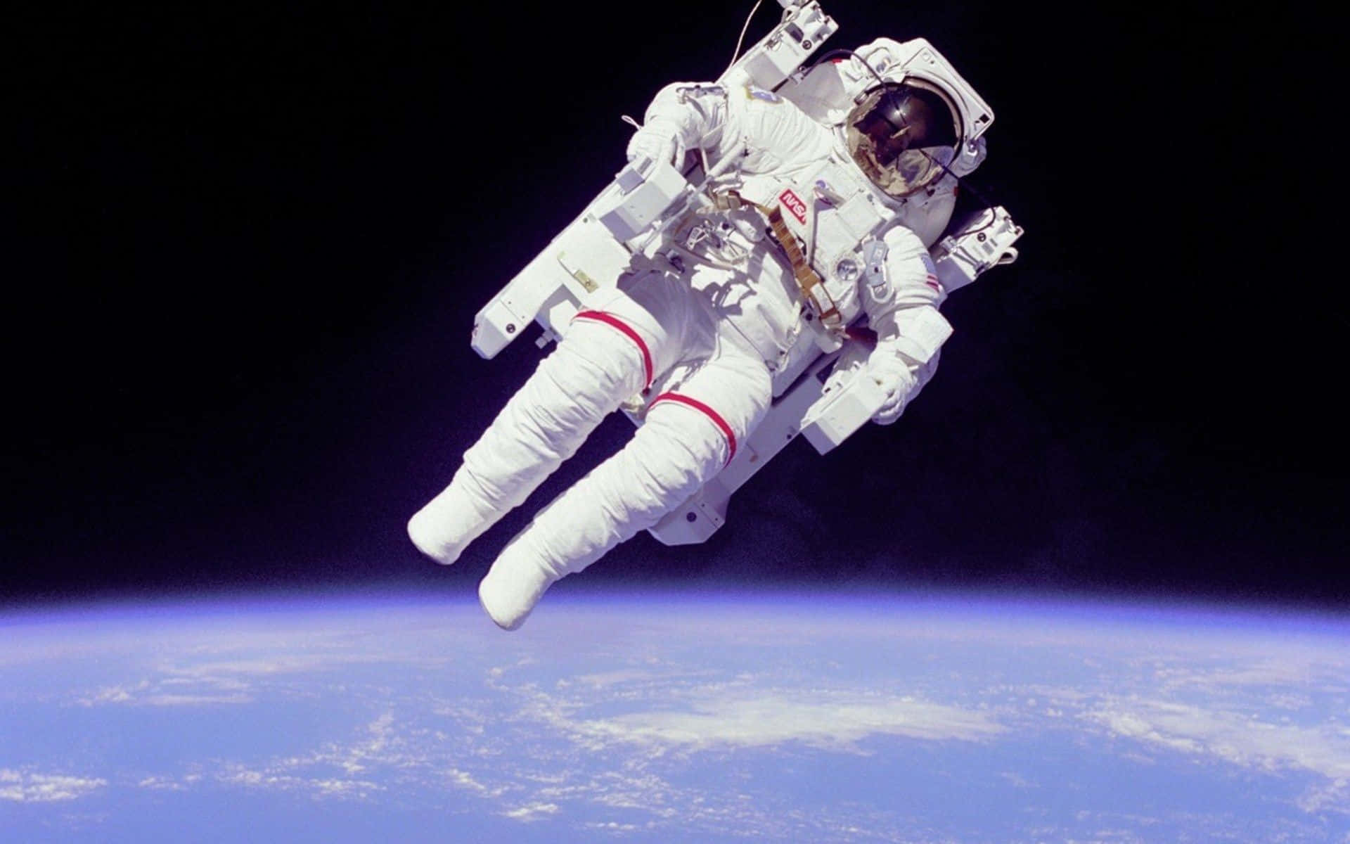 Astronaut Desktop 桌布 壁紙 — 一名太空人在地球彎曲的藍色地平線上方，對著太空的黑色虛空無重力漂浮。