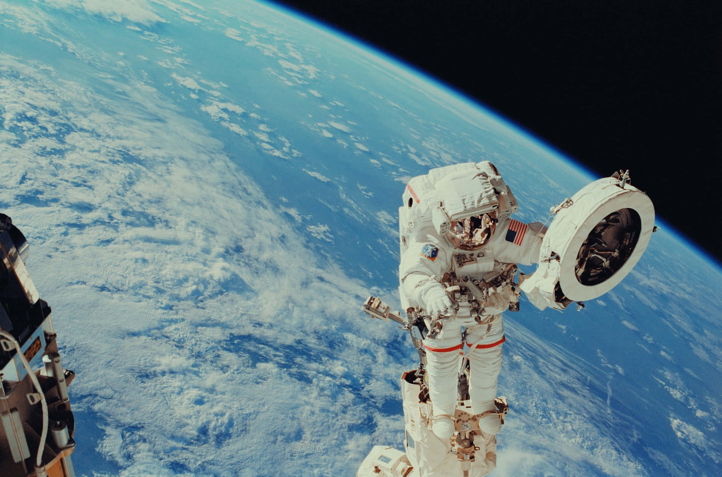 Space Mission 桌布 壁紙 — 一名太空人在太空船外漂浮於太空中，地球的藍色海洋和白色雲朵在下方彎曲。
