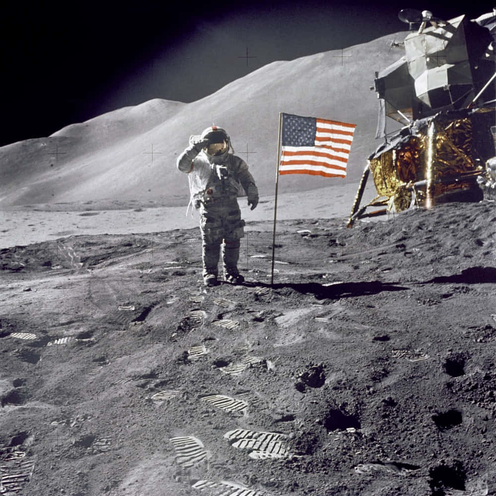 Moon Landing 桌布 壁紙 — 一名太空人在月球塵土飛揚的表面旁，向飄揚的美國國旗敬禮，附近有月球登陸器。