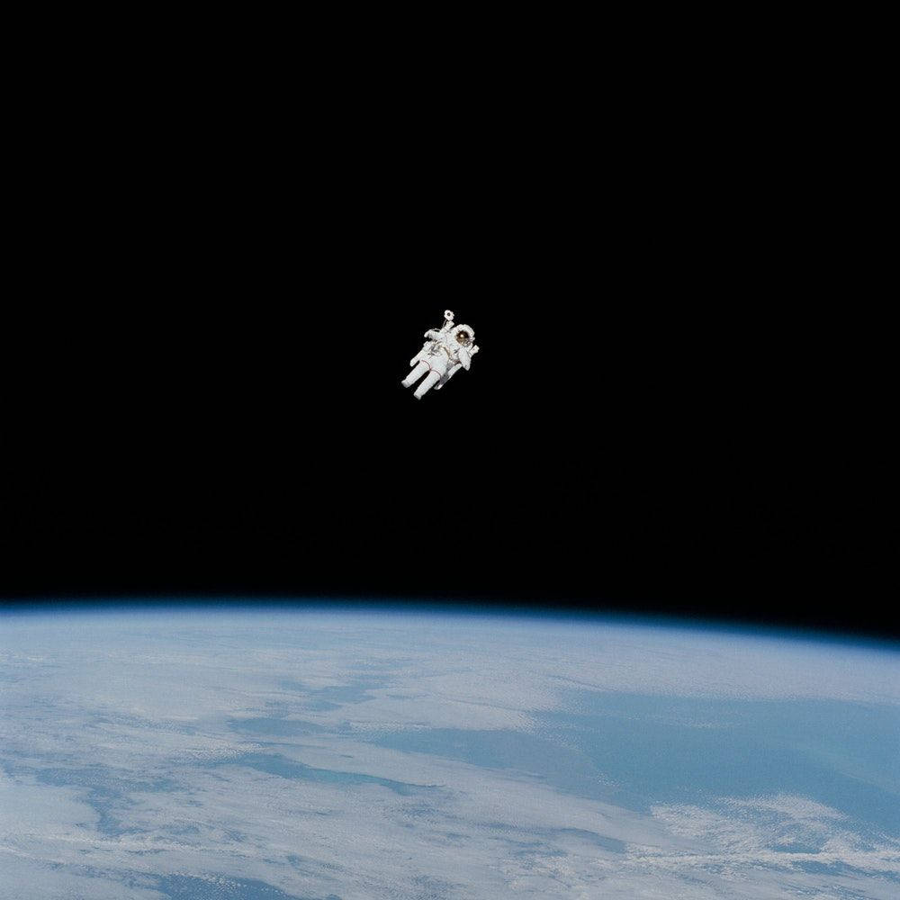 NASA 動態圖片 桌布 壁紙 — 一名太空人在零重力下漂浮在地球彎曲的藍白大氣層之上，背景是太空的黑色虛空。